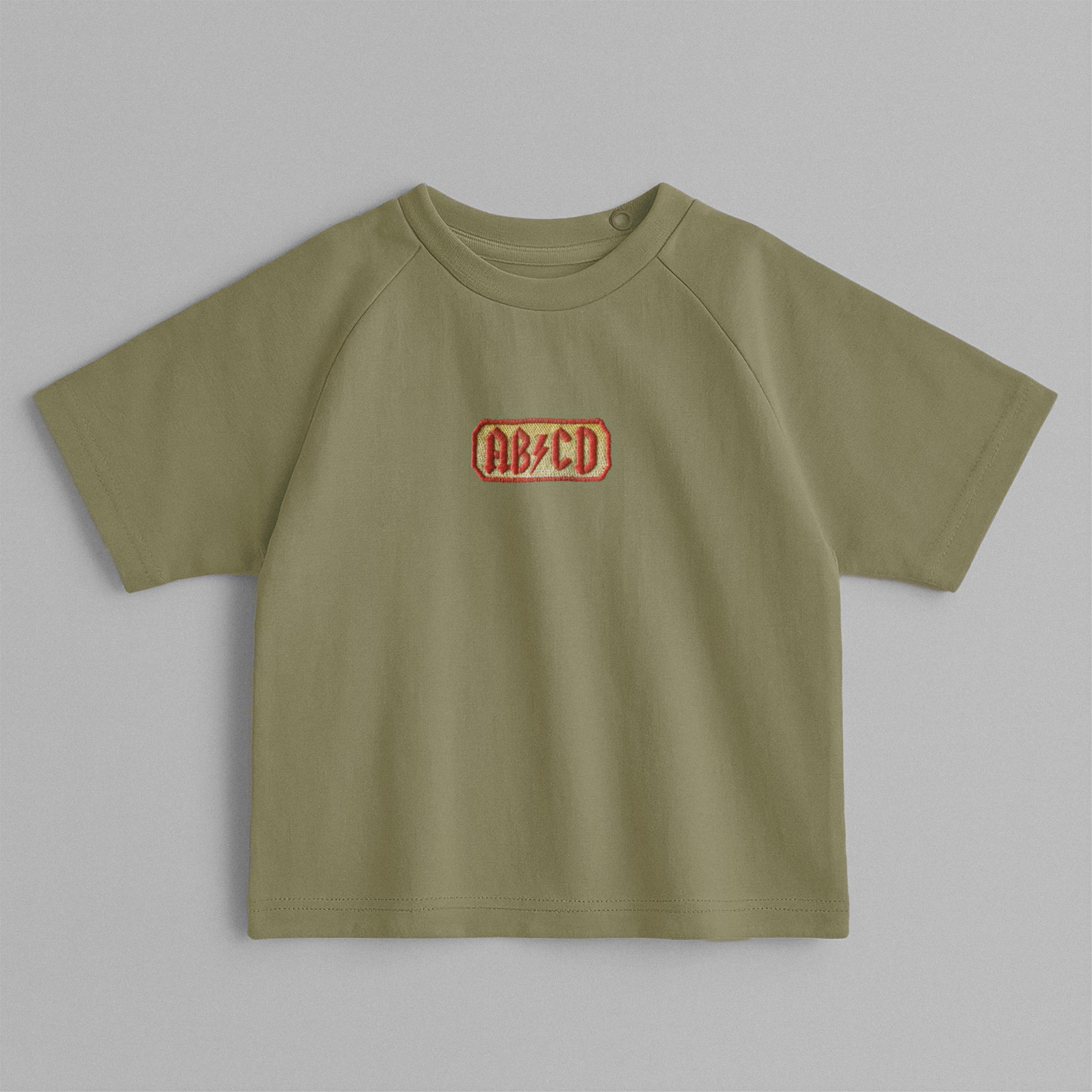 Haki yeşili, reglan kollu, omuzdan çıtçıtlı bebek tişörtü. Göğüs kısmında AC/DC logosu stilinde "AB/CD" nakışı bulunmaktadır.