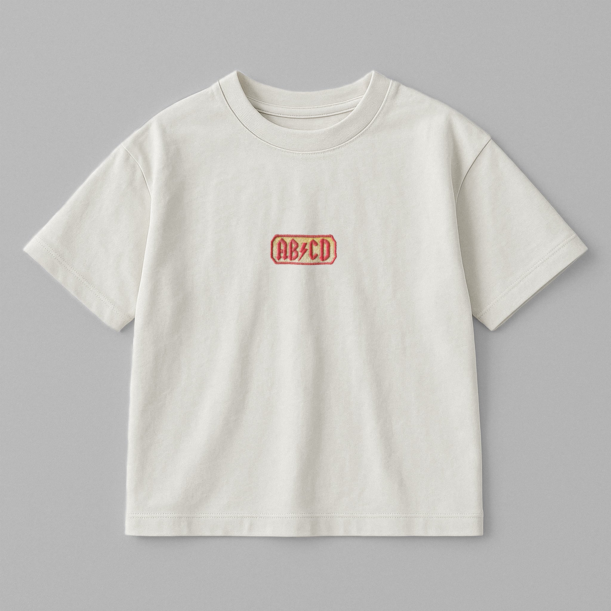 Ekru renkli, oversize kesim, 1-5 yaş için pamuklu çocuk tişörtü. Göğüs kısmında AC/DC logosu stilinde "AB/CD" nakışı bulunmaktadır.