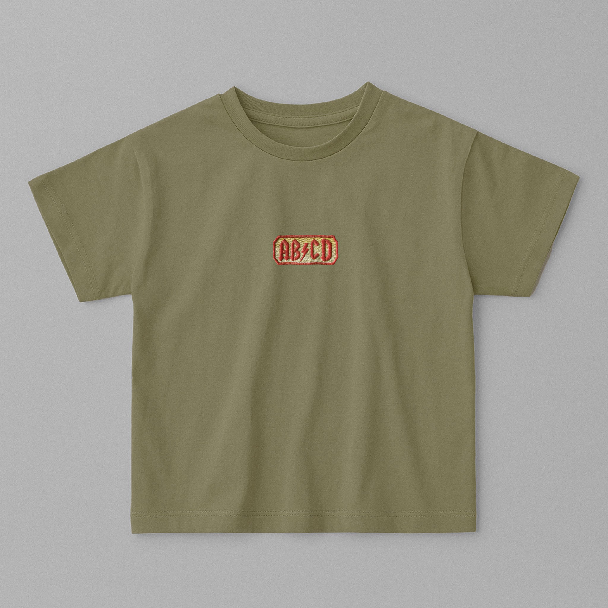 Haki yeşili, oversize kesim, 1-5 yaş için pamuklu çocuk tişörtü. Göğüs kısmında AC/DC logosu stilinde "AB/CD" nakışı bulunmaktadır.