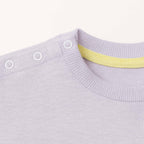 Lila renkli bebek sweatshirt'ünün omuz kısmındaki beyaz çıtçıtların ve yaka içindeki sarı biyenin yakın plan kalite detayı fotoğrafı.