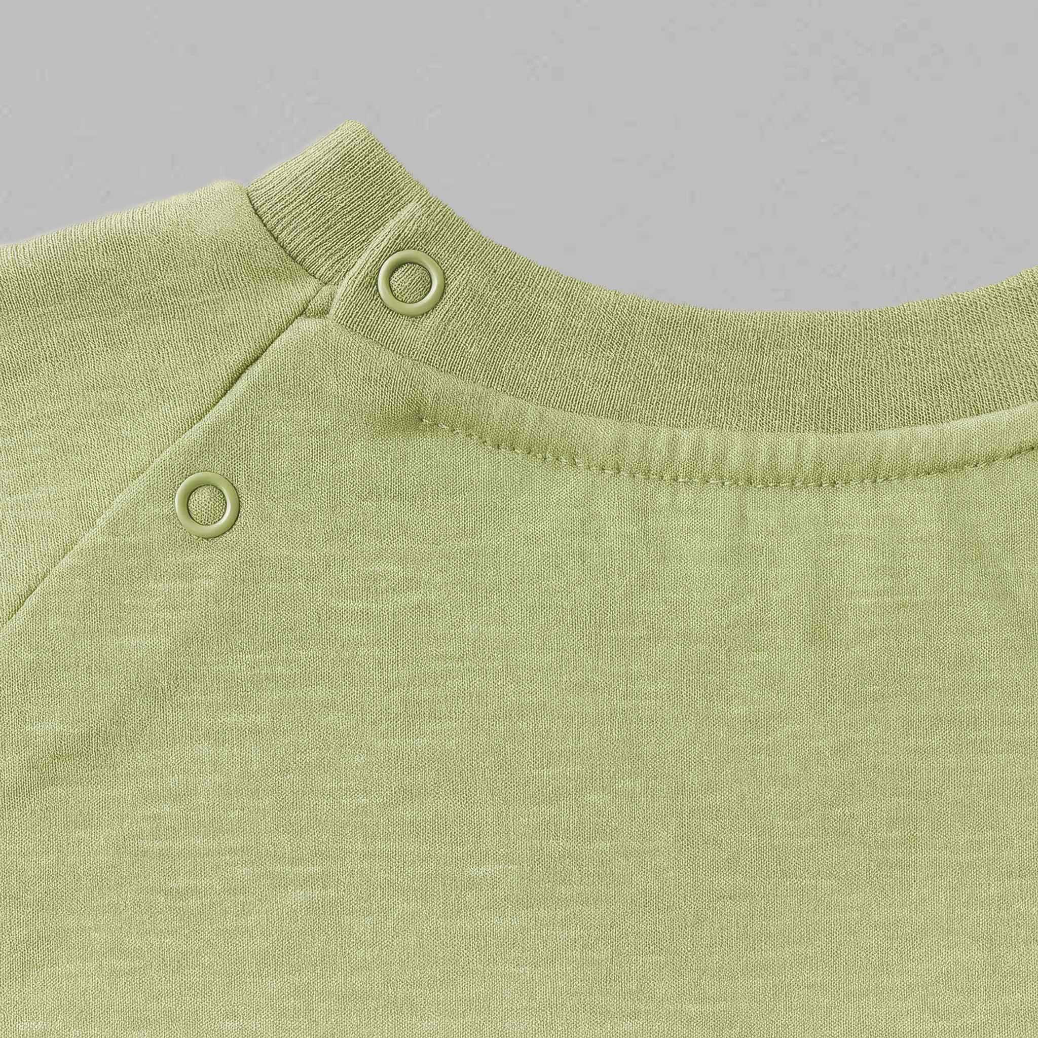 Yeşil renkli pamuklu bebek tişörtünün omuz kısmındaki iki adet çıtçıtın ve dikiş detaylarının yakın çekim kalite fotoğrafı.