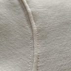 Oversized ekru hoodie modelindeki beyaz ipin dokusunu ve ucunu gösteren detay çekim. Woven (dokuma) yapısı ve minimalist tasarıma eşlik eden kaliteli aglet detayı. Şıklık ve fonksiyonelliği bir arada sunan beyaz ipin ekru kumaşla buluşması.