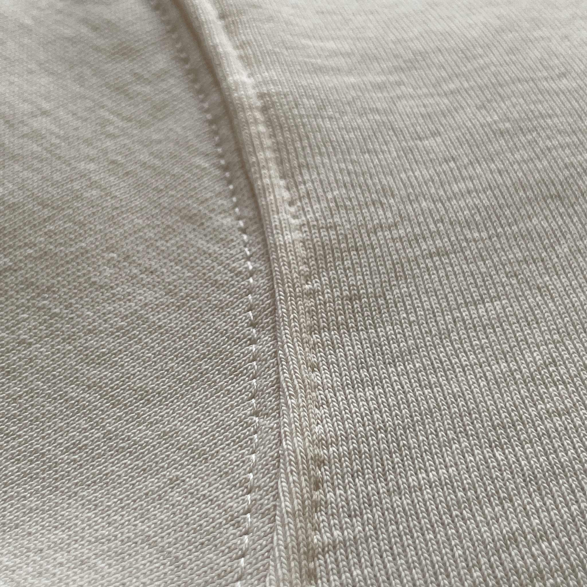 Oversized ekru hoodie modelindeki beyaz ipin dokusunu ve ucunu gösteren detay çekim. Woven (dokuma) yapısı ve minimalist tasarıma eşlik eden kaliteli aglet detayı. Şıklık ve fonksiyonelliği bir arada sunan beyaz ipin ekru kumaşla buluşması.