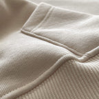 Yetişkinler için kapüşonlu beyaz hoodie modelinin minimalist cep dikişini ve kumaş dokusunu gösteren yakın çekim. Kaliteli tok kumaşın örgü dokusu ve temiz işçilikle hazırlanmış cep kenar detayı. Şıklık ve konfor sunan cep tasarımının temel dikiş izi.