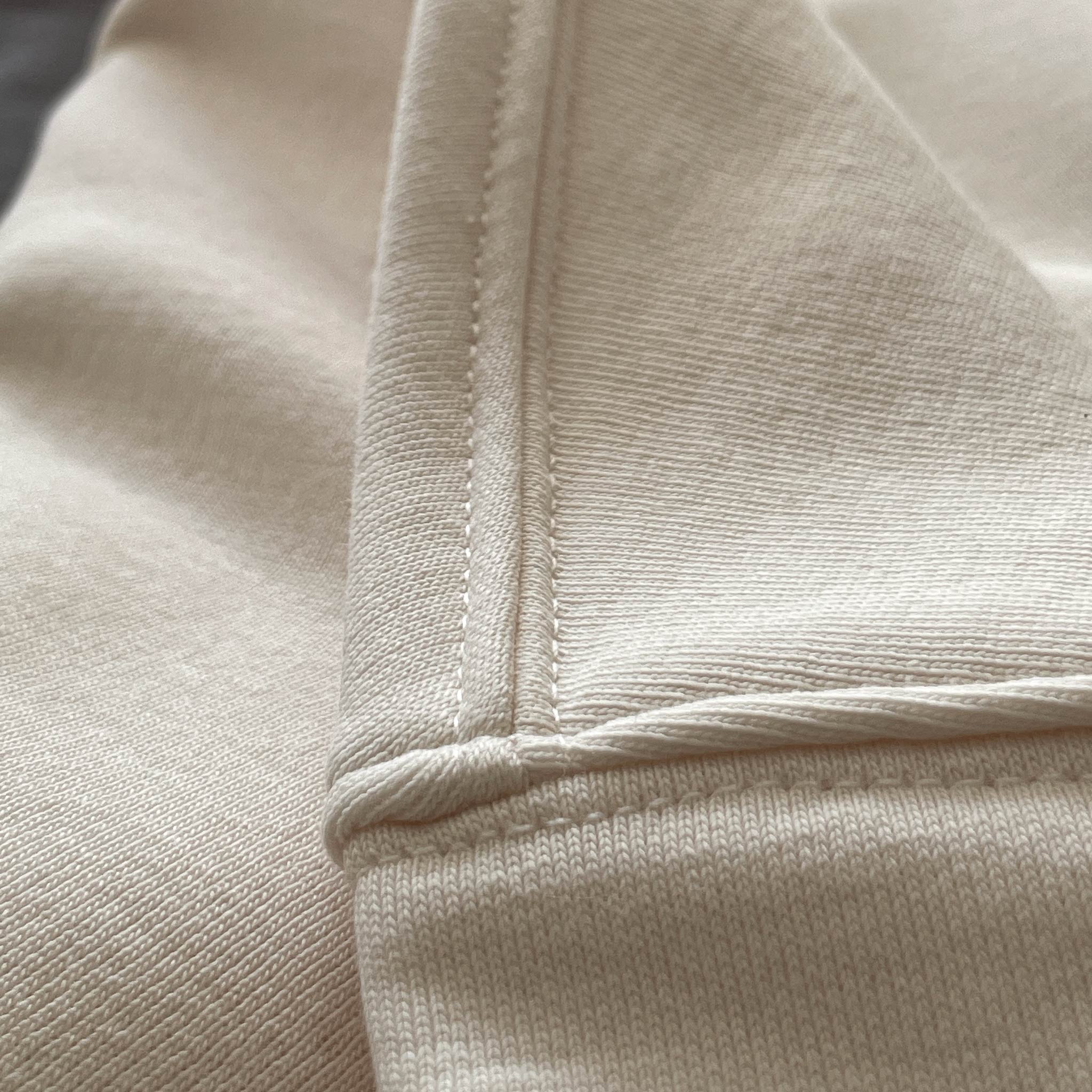 Beyaz renkli premium yetişkin hoodie modelinin omuz dikişi ile kol evi birleşim noktasını gösteren makro detay çekimi. Kaliteli tok kumaş ve kusursuz çoklu reçme dikiş işçiliği, dökümlü oversized kalıbın formunu uzun süre korumasını sağlayan yapısal sağlamlık. Şıklık ve dayanıklılık sunan temel işçilik detayı.