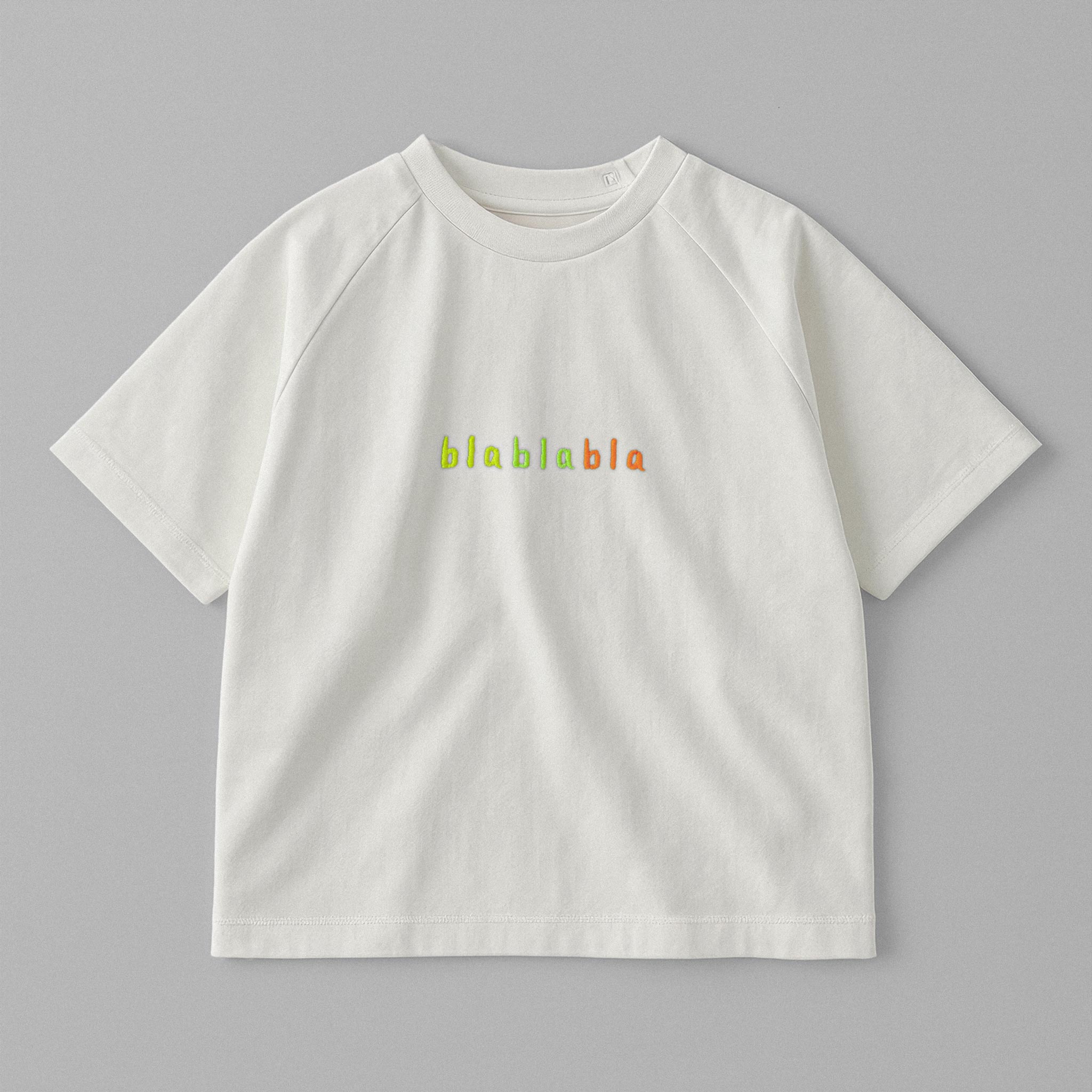 Ekru renkli, reglan kollu, omuzdan çıtçıtlı bebek tişörtü. Göğüs kısmında renkli ipliklerle "blablabla" nakışı bulunmaktadır.