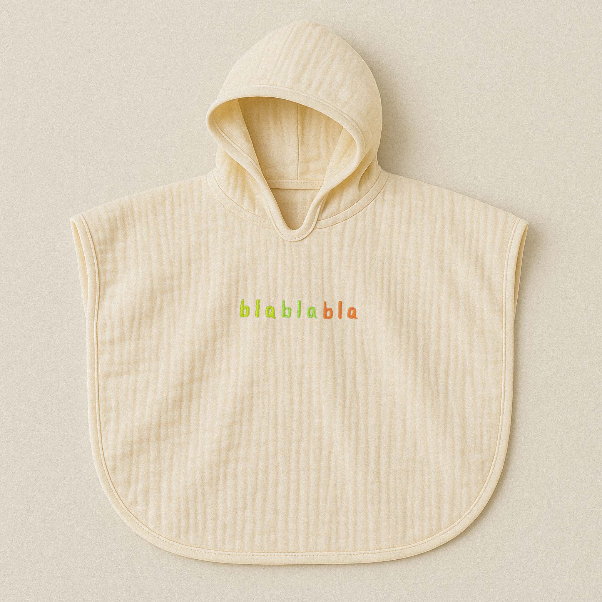 Ekru (doğal bej) renginde, kapüşonlu, müslin kumaştan bebek ve çocuk pançosu. Göğüs kısmında renkli ipliklerle "blablabla" yazısı işlenmiştir.