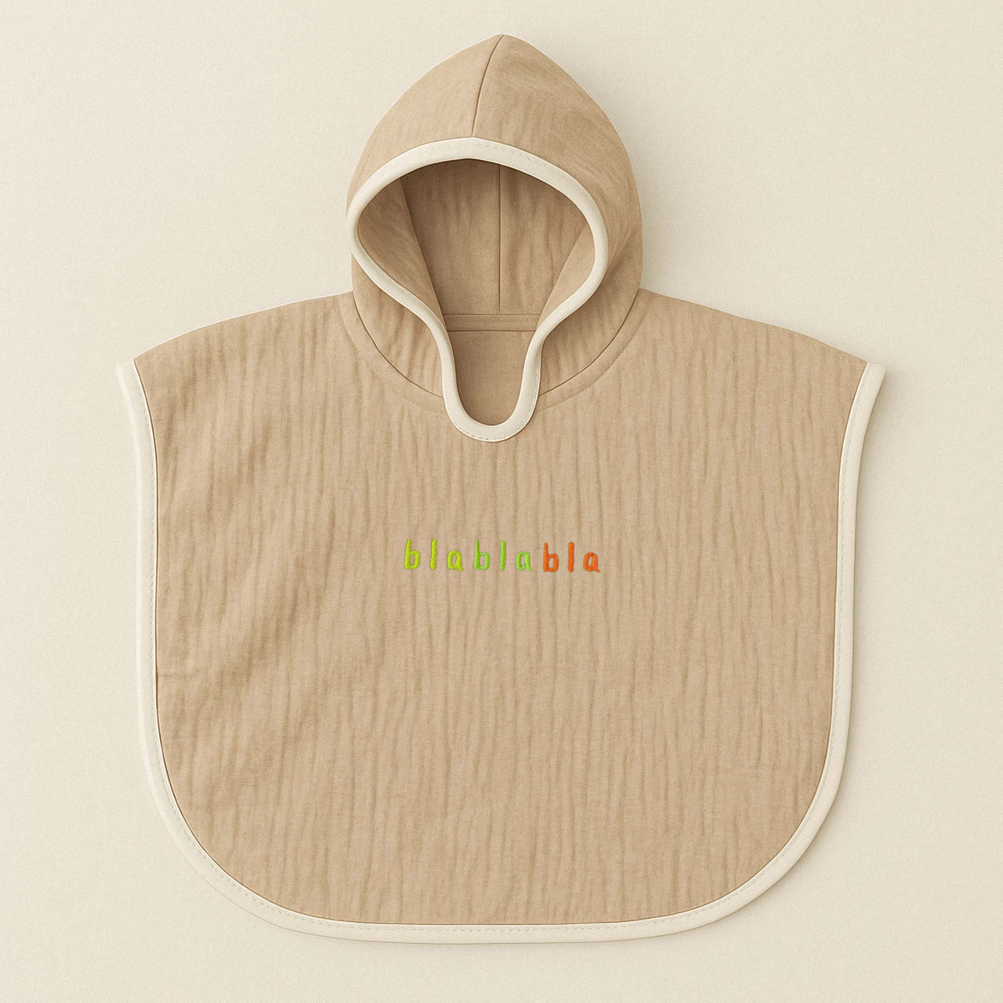 Somon rengi (bej), kapüşonlu, müslin kumaştan bebek ve çocuk pançosu. Göğüs kısmında renkli ipliklerle "blablabla" yazısı işlenmiştir.