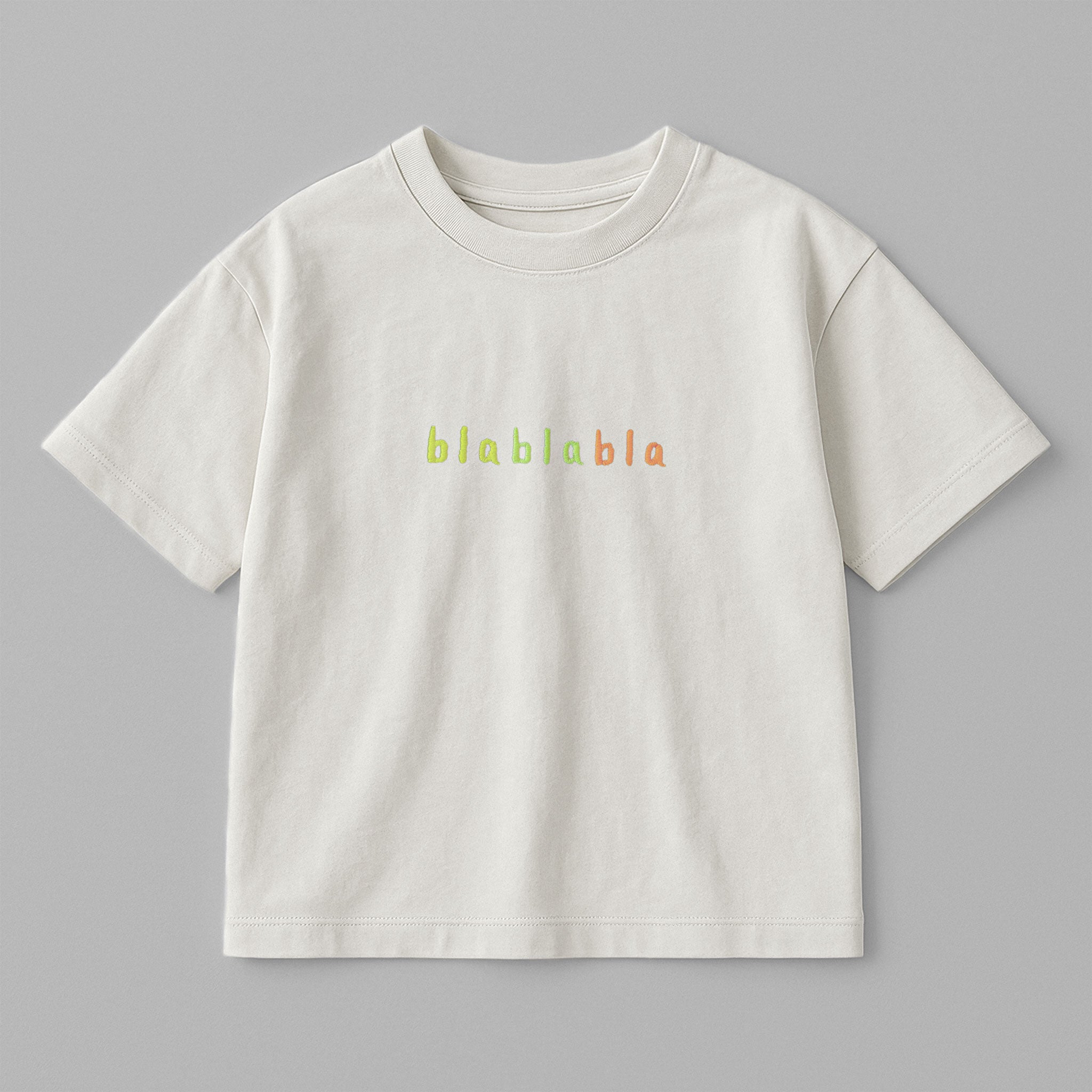 Ekru renkli, oversize kesim, 1-5 yaş için pamuklu çocuk tişörtü. Göğüs kısmında renkli ipliklerle "blablabla" nakışı bulunmaktadır.