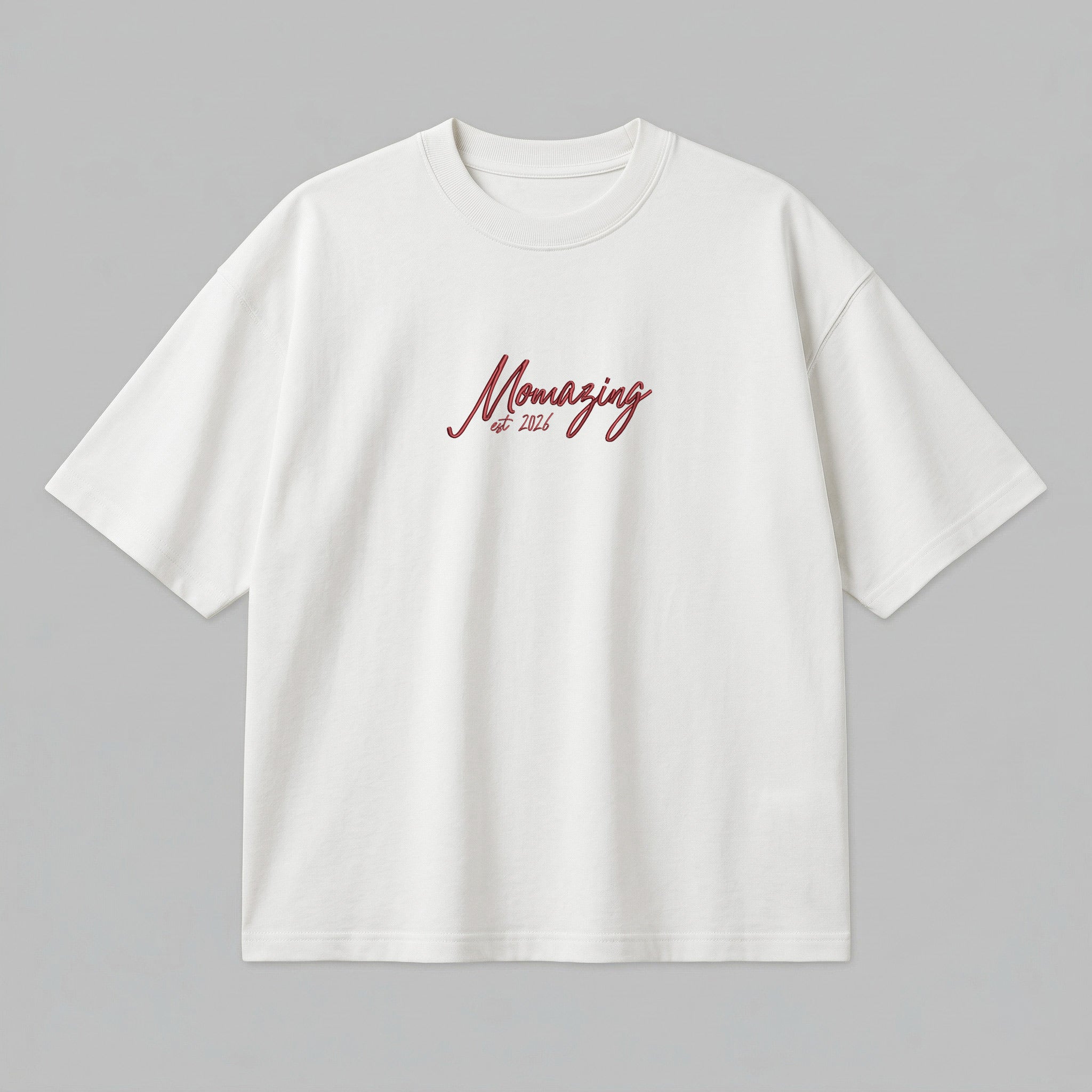 Yetişkinler için ekru (krem) renkli premium loose fit kesim pamuk t-shirt kapak görseli. Sol göğüste kırmızı el yazısı fontuyla "Momazing est. 2026" nakış örneği yer alır. Bu model, anne olma yılınızı (maks. 8 karakter) Alman nakış kalitesiyle özelleştirerek size özel bir parça oluşturmanızı sağlar. %100 pamuklu, heavyweight tok kumaşı formunu korurken loose fit kesim ile gün boyu konfor ve stil sunar. Kendinize has bir premium giyim ürünü tasarlamak için mükemmeldir.