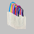 Açık mavi, sarı, fuşya, saks mavisi, kırmızı, mor ve siyah renkli omuz askısı seçenekleriyle yan yana dizilmiş ham kanvas tote bag (bez çanta) serisi. Günlük kullanıma uygun, kişiselleştirilebilir nakış tasarımlarına zemin oluşturan şık, sağlam ve çok amaçlı premium kanvas çantalar.