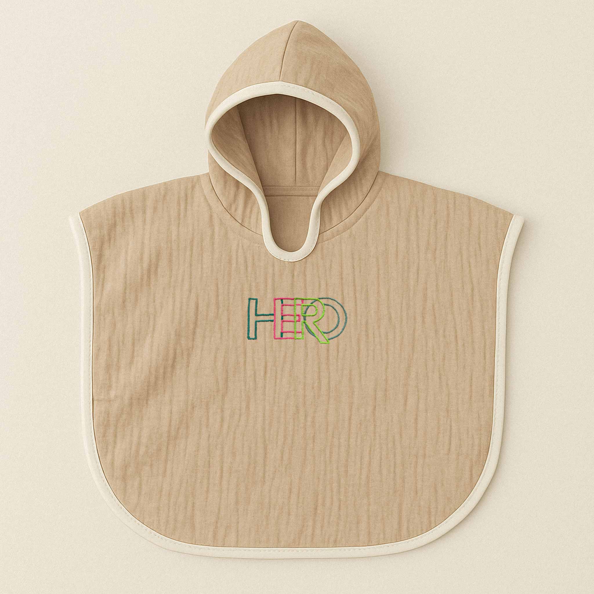 Somon rengi (bej), kapüşonlu, müslin kumaştan bebek ve çocuk pançosu. Göğüs kısmında renkli ipliklerle "HERO" yazısı işlenmiştir.