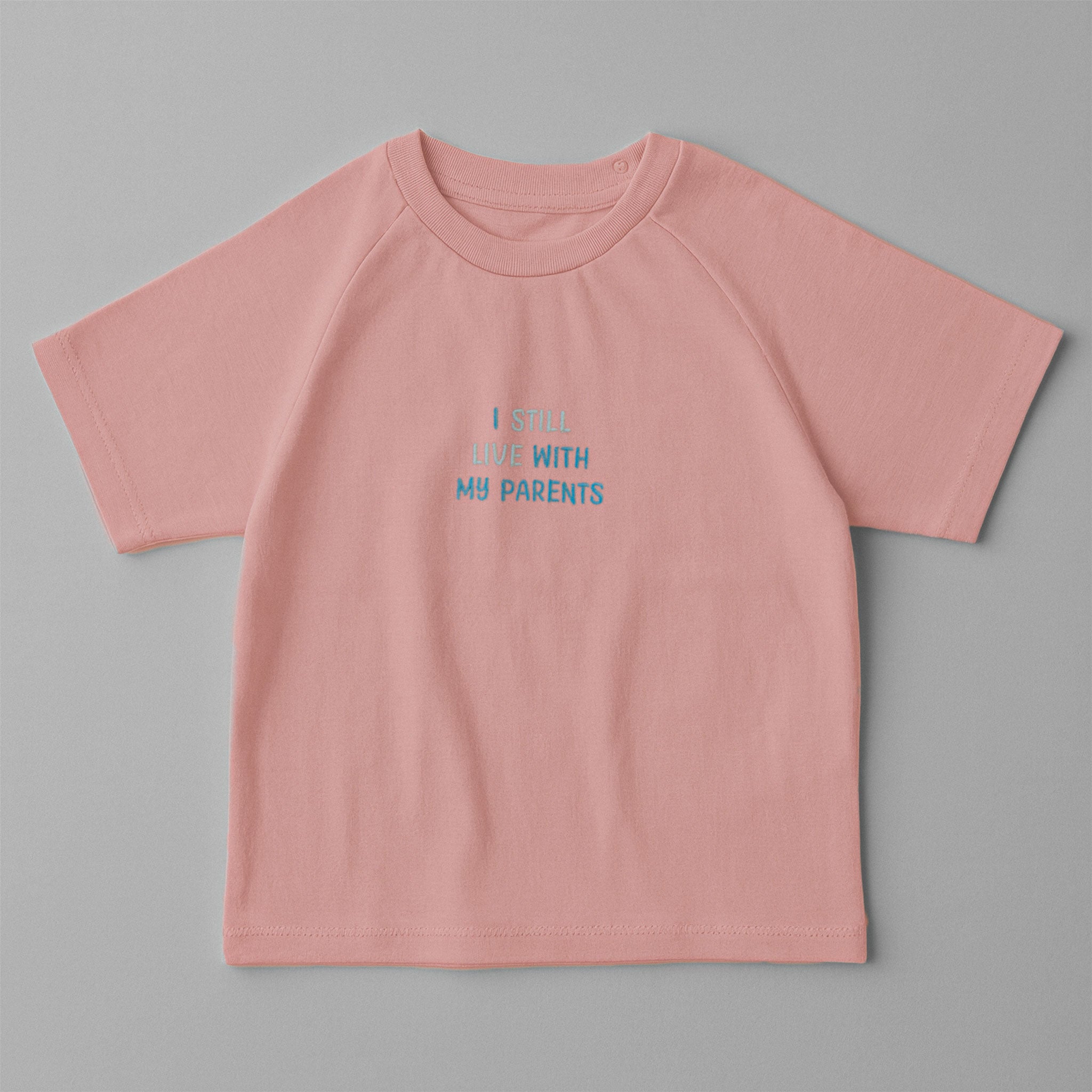 Gül kurusu (pembe) renkli, reglan kollu, omuzdan çıtçıtlı bebek tişörtü. Göğüs kısmında mavi tonlarda "I STILL LIVE WITH MY PARENTS" nakışı bulunmaktadır.