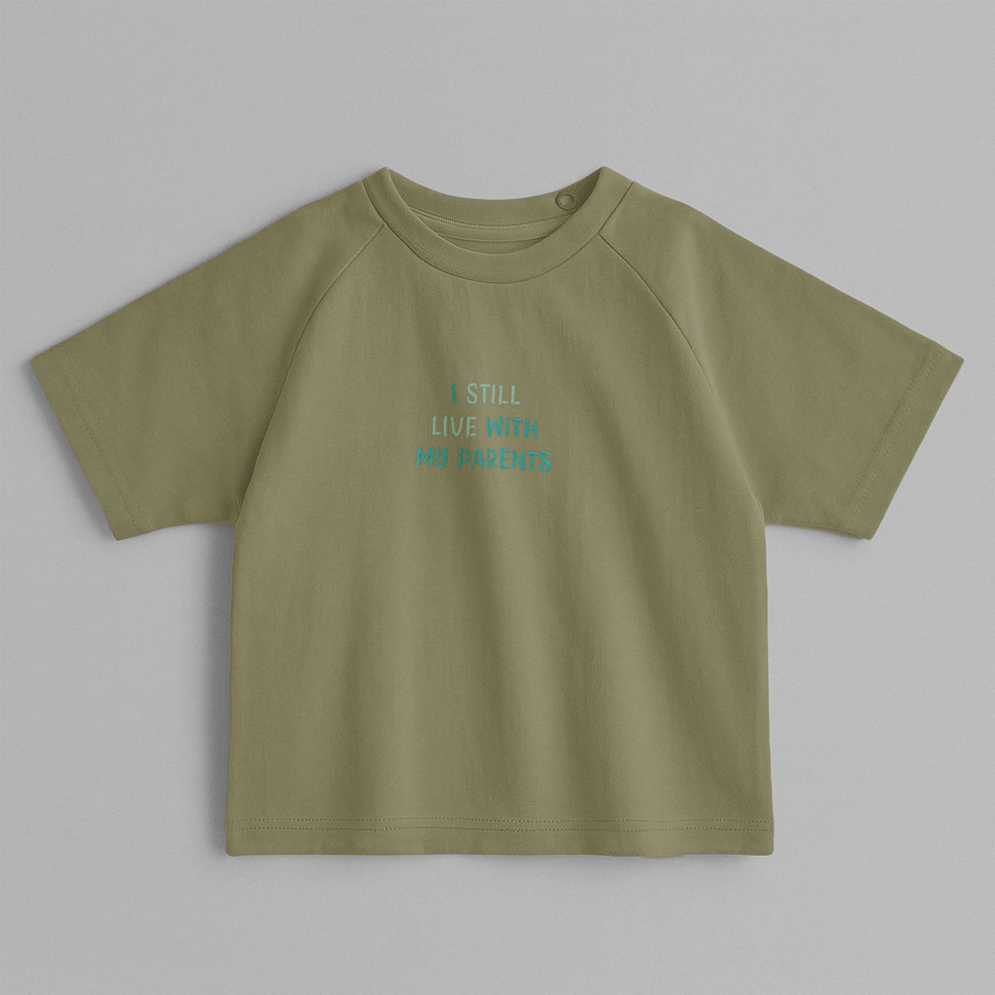 Haki yeşili, reglan kollu, omuzdan çıtçıtlı bebek tişörtü. Göğüs kısmında mavi tonlarda "I STILL LIVE WITH MY PARENTS" nakışı bulunmaktadır.