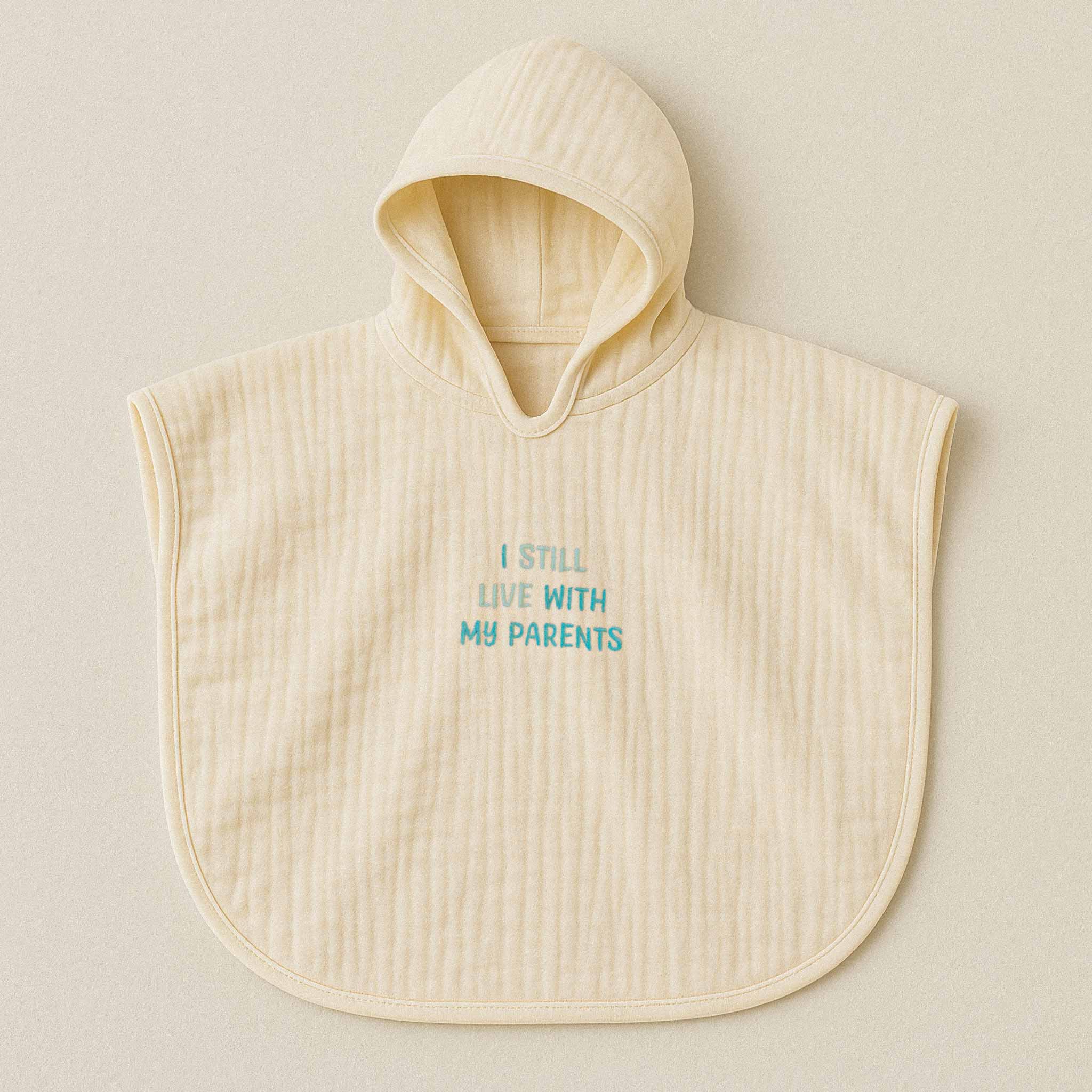 Ekru (doğal bej) renginde, kapüşonlu, müslin kumaştan bebek ve çocuk pançosu. Göğüs kısmında mavi ipliklerle "I STILL LIVE WITH MY PARENTS" yazısı işlenmiştir.