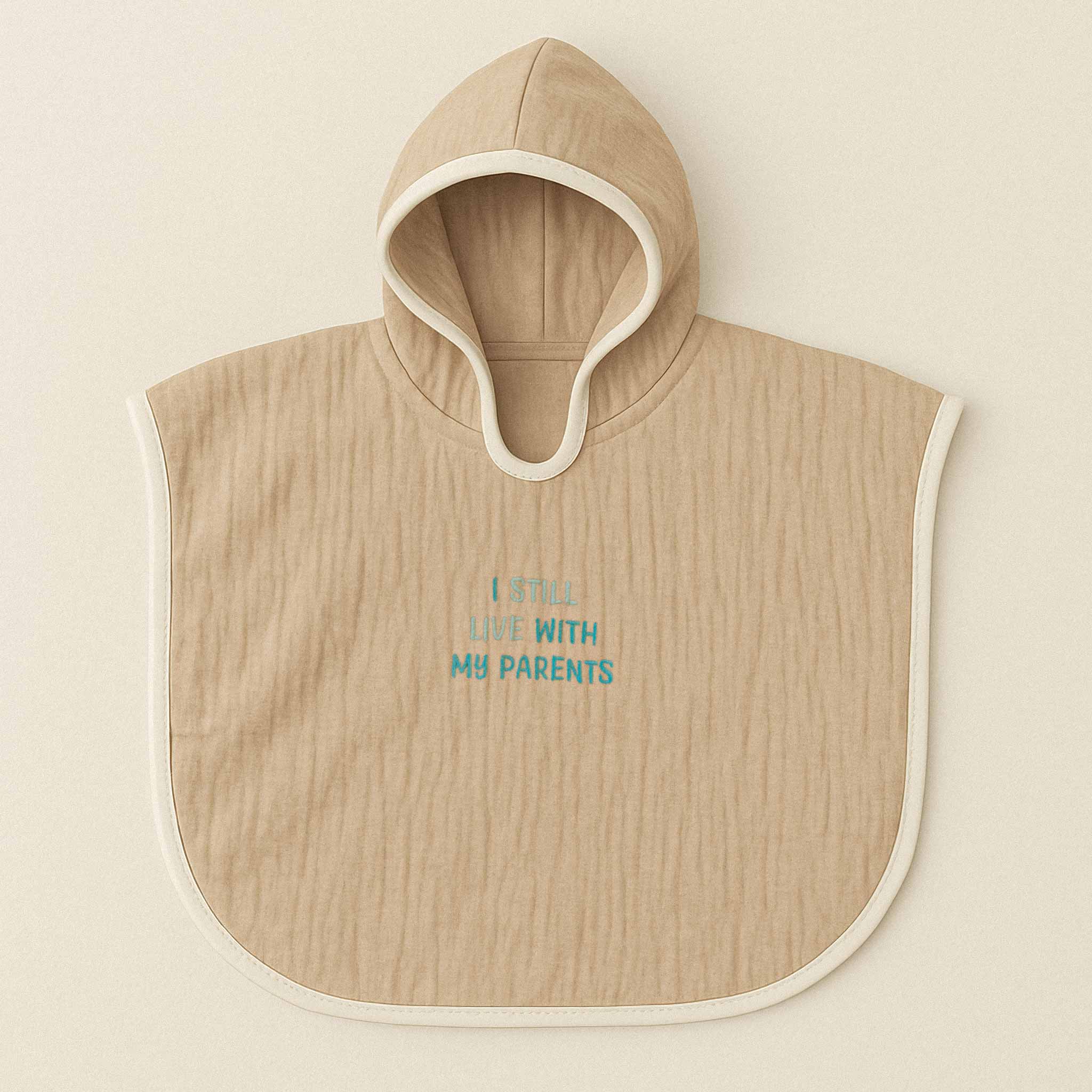 Somon rengi (bej), kapüşonlu, müslin kumaştan bebek ve çocuk pançosu. Göğüs kısmında mavi ipliklerle "I STILL LIVE WITH MY PARENTS" yazısı işlenmiştir.