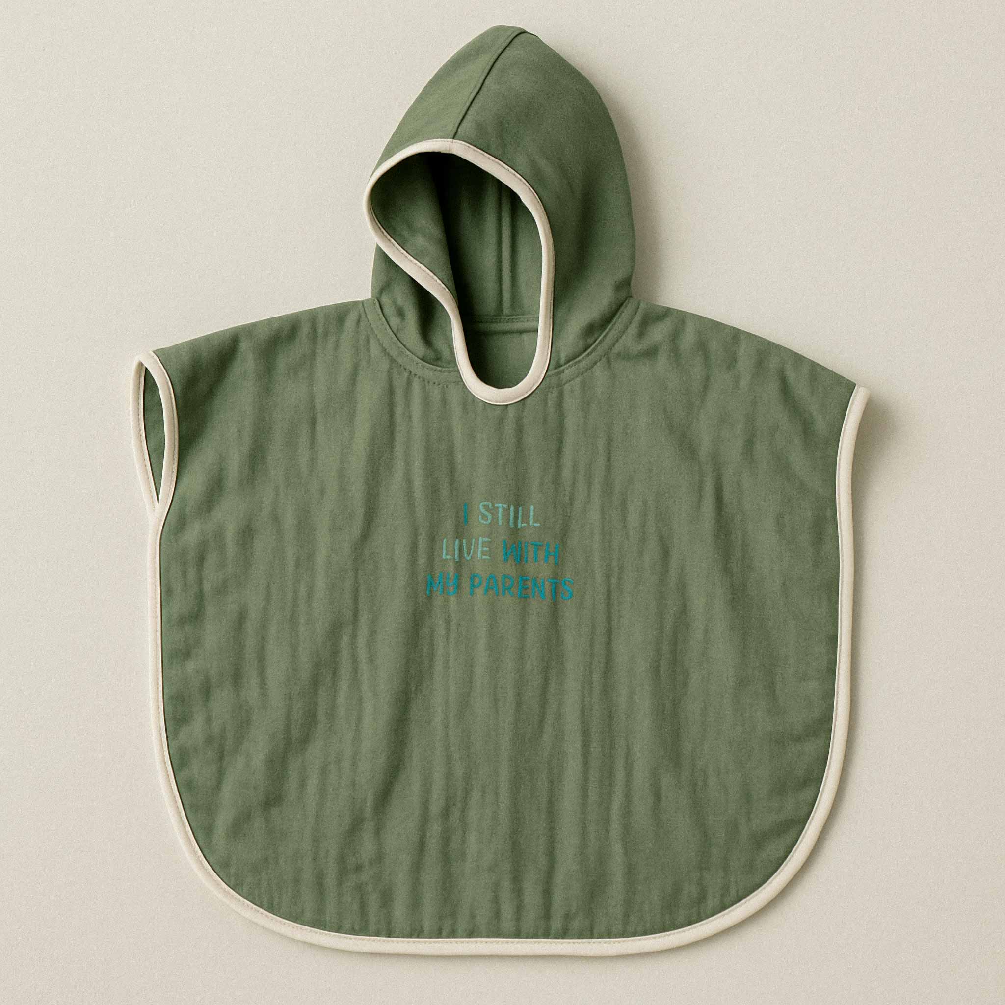 Haki yeşili renginde, kapüşonlu, müslin kumaştan bebek ve çocuk pançosu. Göğüs kısmında mavi ipliklerle "I STILL LIVE WITH MY PARENTS" yazısı işlenmiştir.