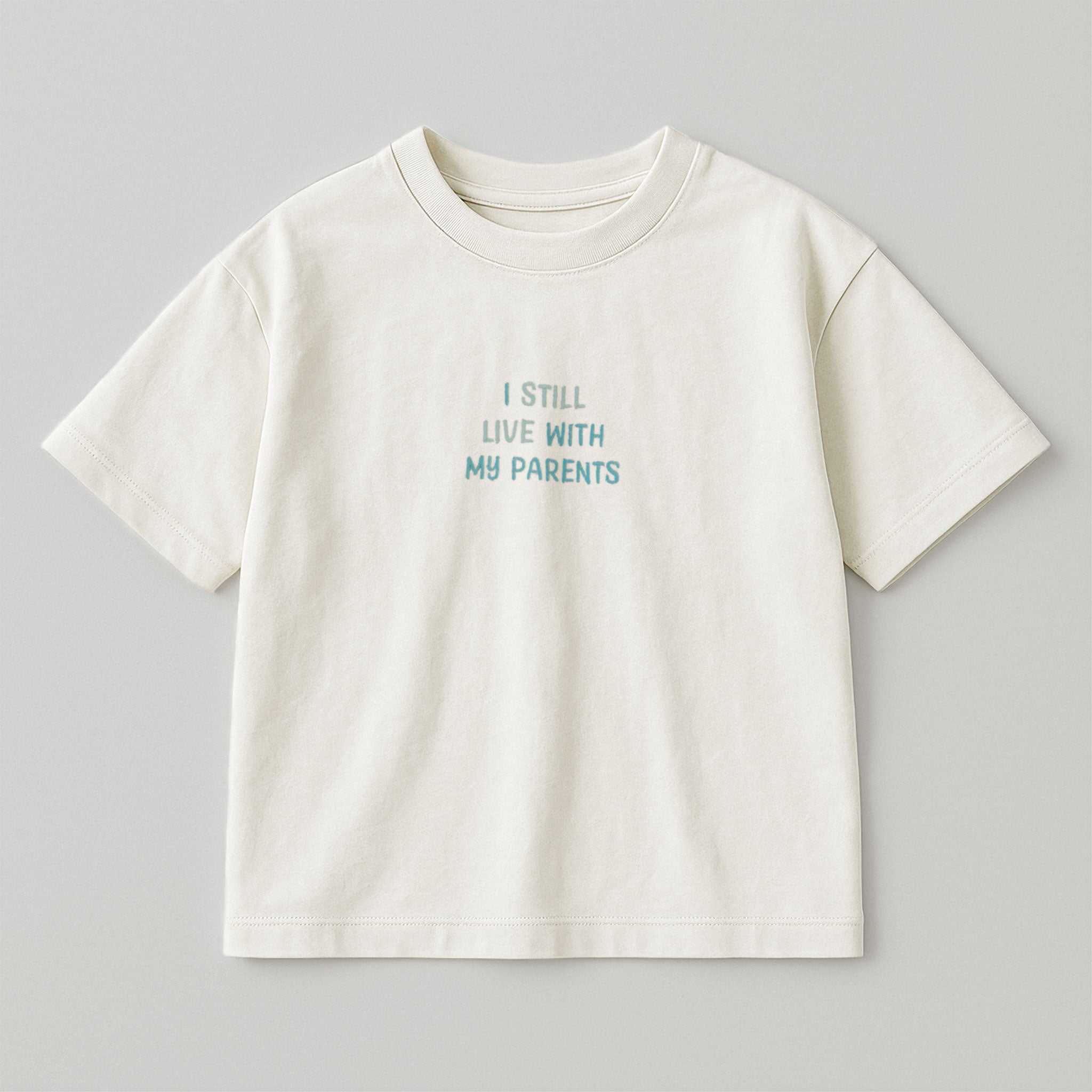 Ekru renkli, oversize kesim, 1-5 yaş için pamuklu çocuk tişörtü. Göğüs kısmında mavi tonlarda "I STILL LIVE WITH MY PARENTS" nakışı bulunmaktadır.