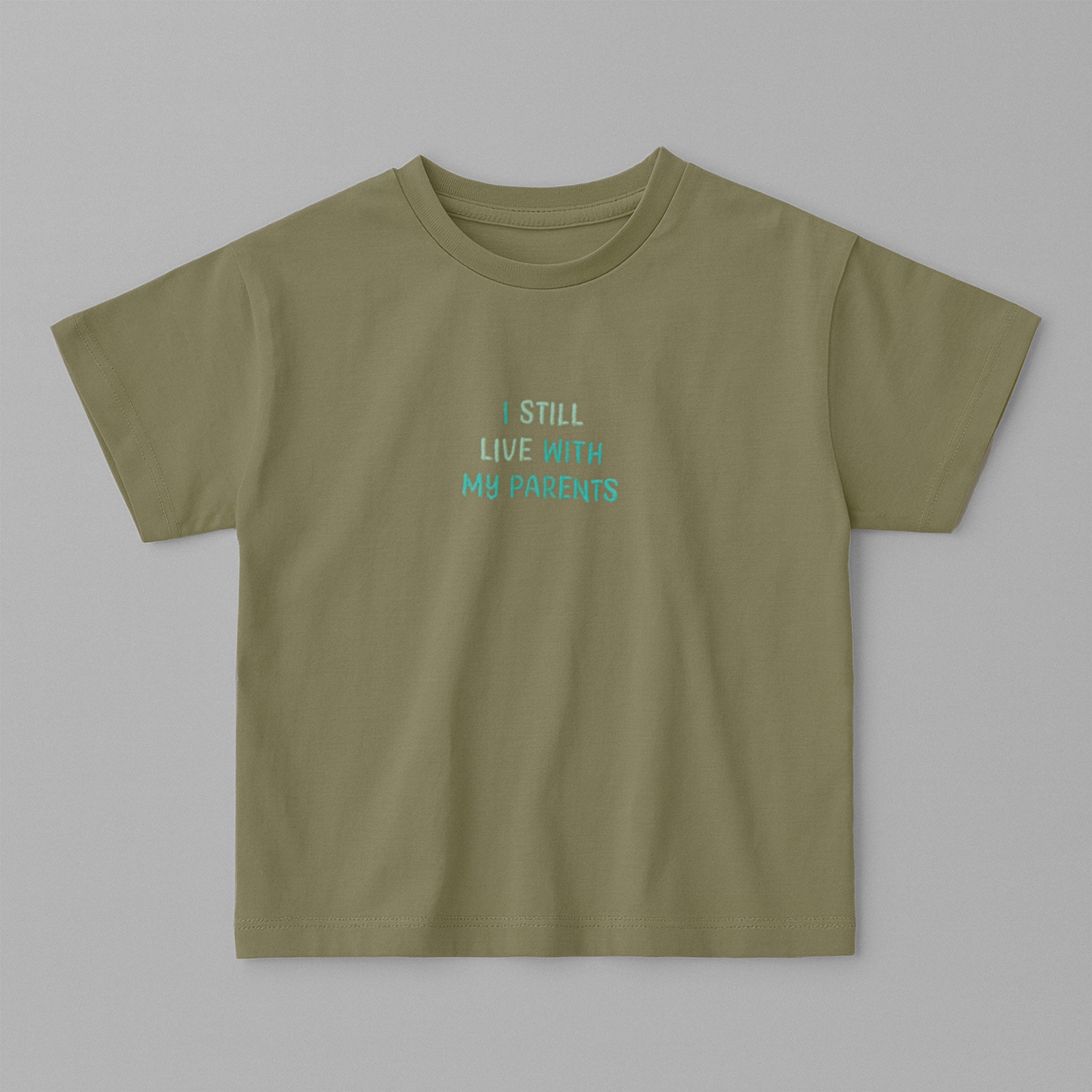 Haki yeşili, oversize kesim, 1-5 yaş için pamuklu çocuk tişörtü. Göğüs kısmında mavi tonlarda "I STILL LIVE WITH MY PARENTS" nakışı bulunmaktadır.