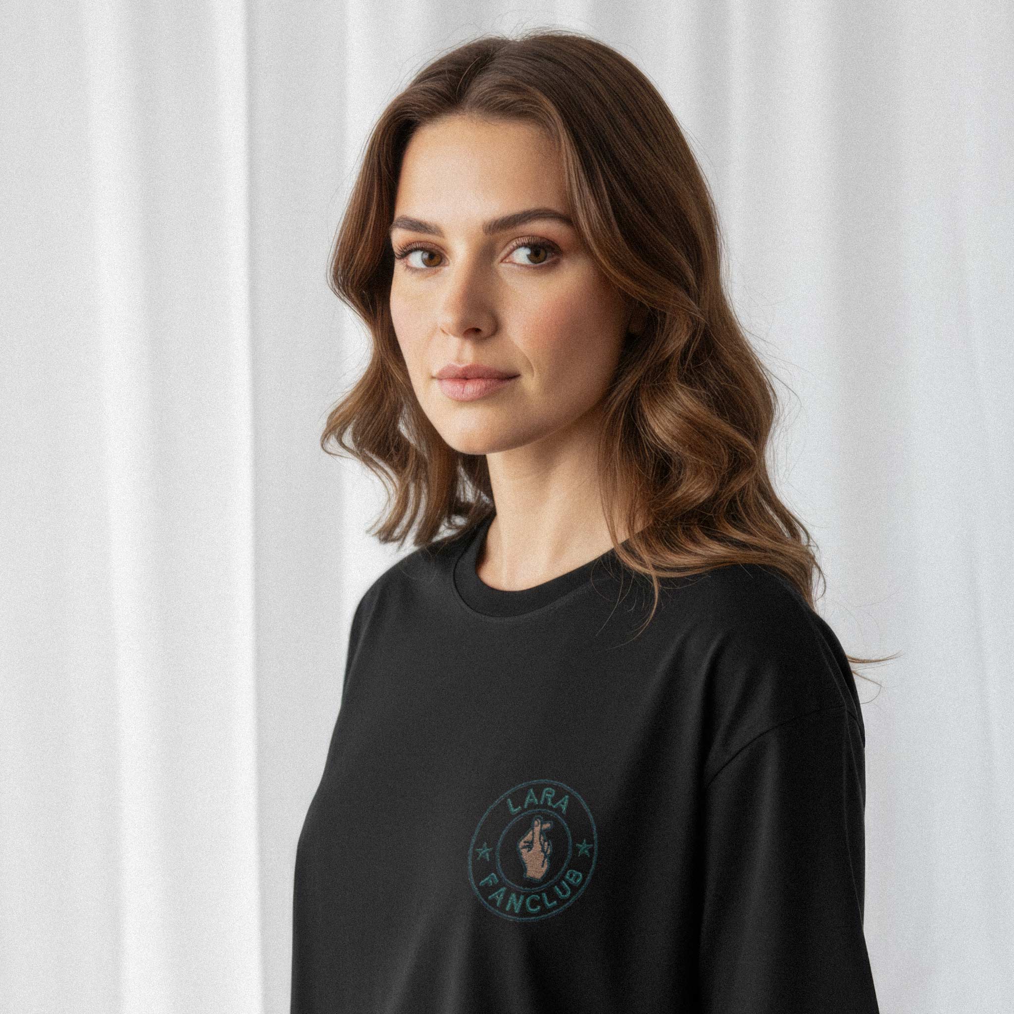 Kadın modelin üzerinde duran siyah renkli, oversize kesim, kişiye özel 'LARA Fanclub' nakışlı Bona Pera tişörtünün yakın plan portre fotoğrafı.