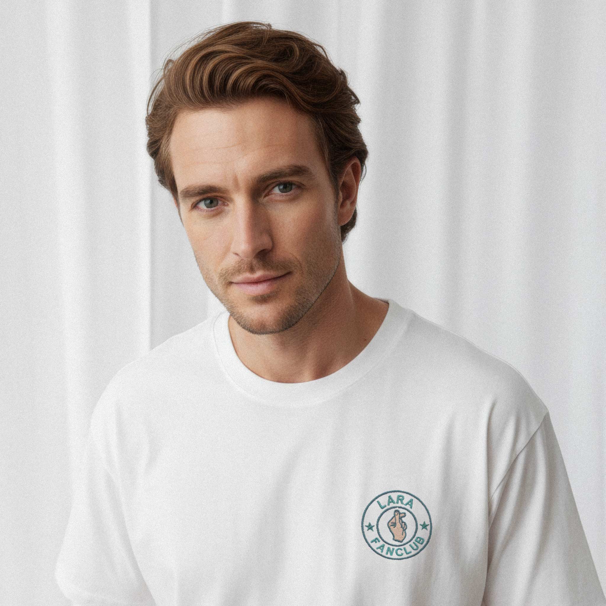 Erkek modelin üzerinde duran beyaz renkli, oversize kesim, kişiye özel 'LARA Fanclub' nakışlı Bona Pera tişörtünün yakın plan portre fotoğrafı.