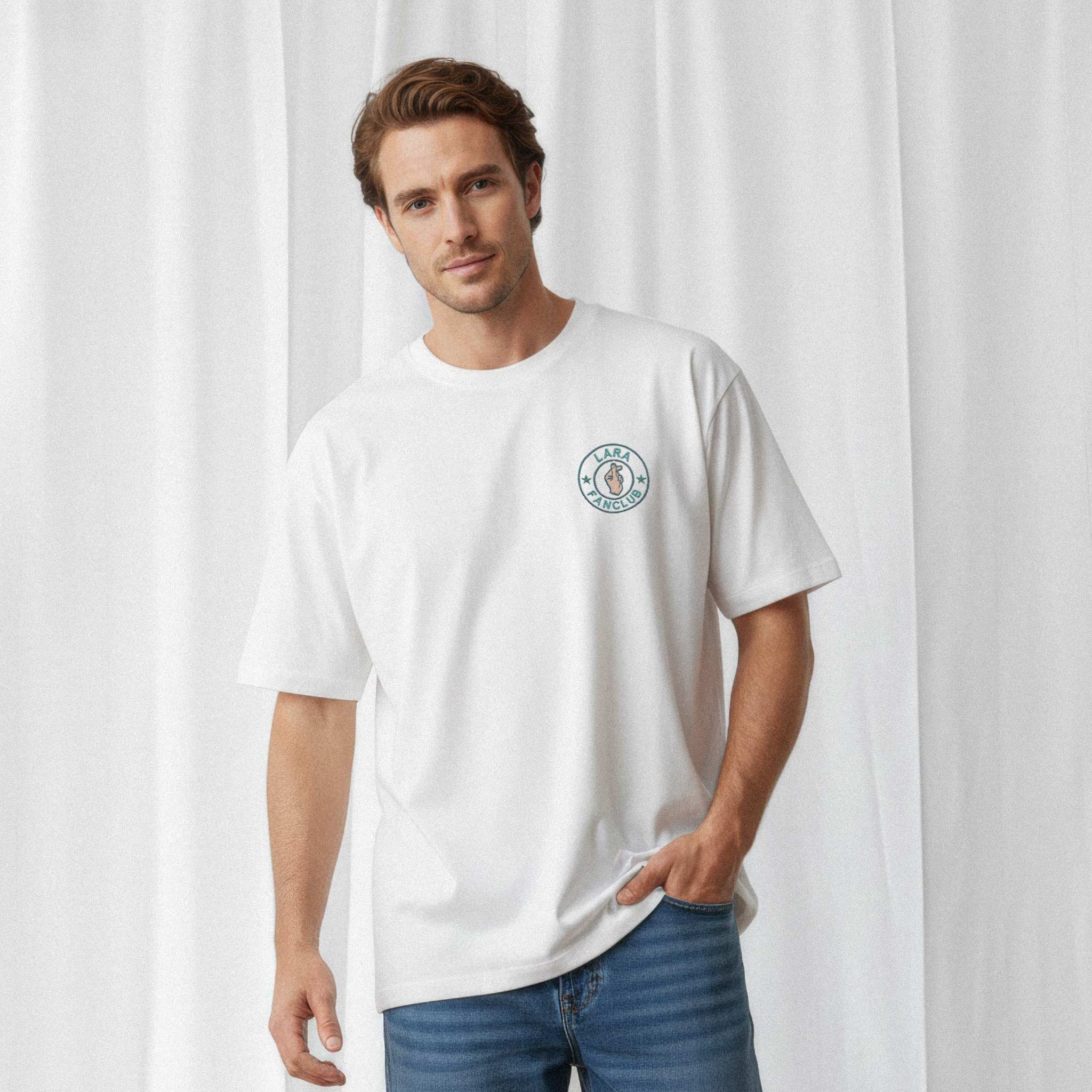 Mavi jean pantolon giyen erkek model, üzerinde Bona Pera'nın beyaz renkli, kişiye özel 'LARA Fanclub' nakışlı oversize tişörtü ile bir eli cebinde poz veriyor.