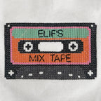 Tişört üzerine cross stitch (çarpı işi) tekniğiyle işlenmiş, 70'ler ve 80'lerin nostaljik sembolü kaset (mix tape) nakışının makro (yakından) görünümü. Pixel art temalı bu renkli ve retro tasarım, üzerine dilediğiniz isim yazılarak tamamen kişiselleştirilebilir. Birinci sınıf Alman nakış ipliği kullanılarak yüksek kalite standartlarında, ince bir işçilikle üretilmiştir. Çocuklar için eğlenceli, nostaljik ve tamamen isme özel premium nakış detayı.