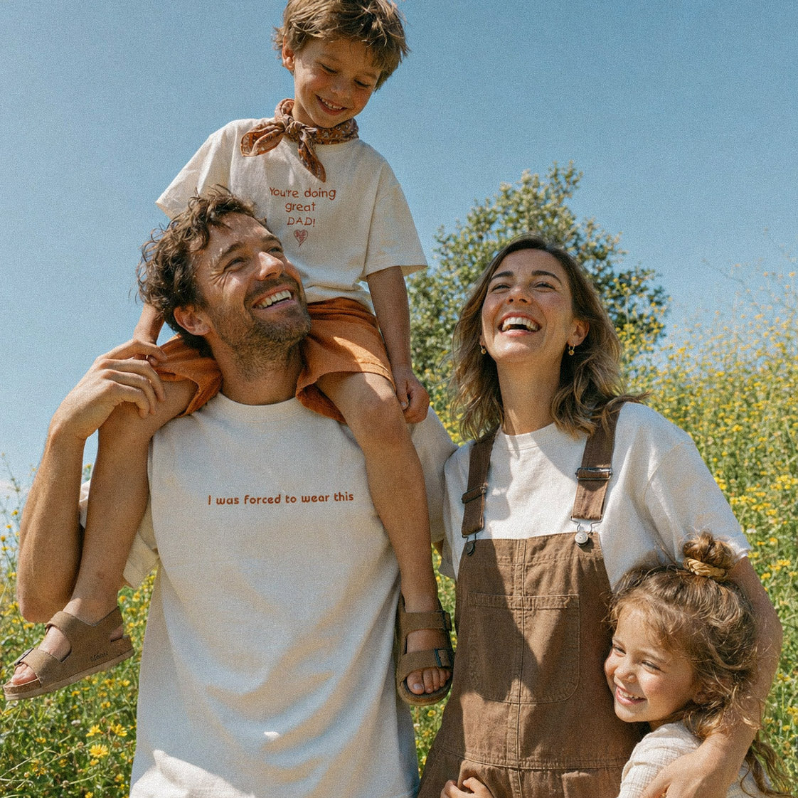 Doğada neşeli aile lifestyle çekimi. Babada "I was forced to wear this", çocukta "You're doing great DAD!" nakışlı kırık beyaz %100 pamuklu oversize tişörtler. Esprili ve premium Alman işçiliği baba-çocuk kombini.