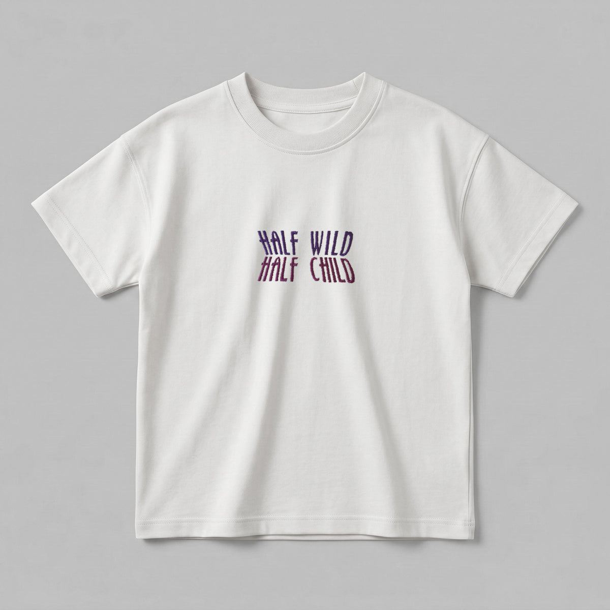 Kırık beyaz renkli, %100 pamuklu Oeko-Tex sertifikalı oversize çocuk t-shirt modeli. Göğüs kısmında mor ve pembe tonlarında geçişli renk efektiyle işlenmiş esprili "HALF WILD HALF CHILD" yazılı nakış detayı yer alır. Birinci sınıf Alman nakış ipliği kullanılarak özenle üretilmiştir. Tok duruşlu heavyweight kumaşı, nefes alan ve terletmeyen yapısıyla çocukların enerjik doğasına uyum sağlayan, premium ve şık günlük giyim parçası.
