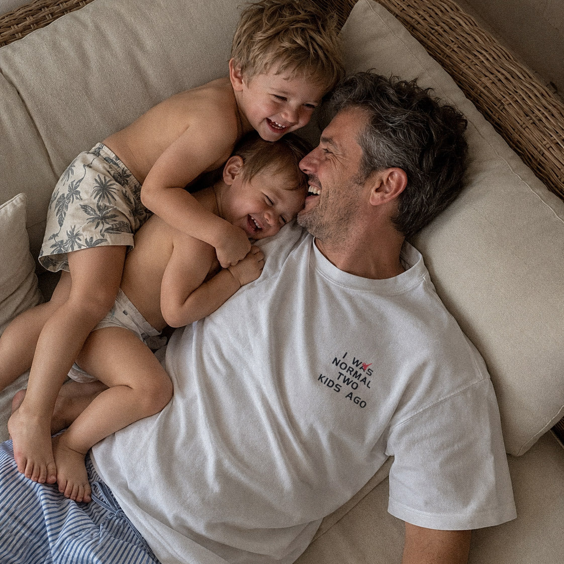 Kırık beyaz renkli %100 pamuklu Oeko-Tex sertifikalı loose fit erkek tişörtü. Sol göğsünde esprili "I WAS NORMAL TWO KIDS AGO" yazısı siyah ve kırmızı iplikle işlenmiştir. Babalık serüvenini anlatan "deadpan" mizah detaylı premium tişörtün ev içi konforlu anlarını yansıtan lifestyle çekimi.