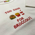 Kırık beyaz renkli %100 pamuklu çocuk oversize tişörtü. Üzerinde kırmızı iplikle işlenmiş "TOO GOOD FOR BROCCOLI!" yazısı ve renkli hamburger, patates kızartması, içecek motiflerinden oluşan nakış tasarımı yer alır. Oeko-Tex sertifikalı kumaşı nefes alan yapısıyla terletmez. Esprili premium günlük giyim parçası.