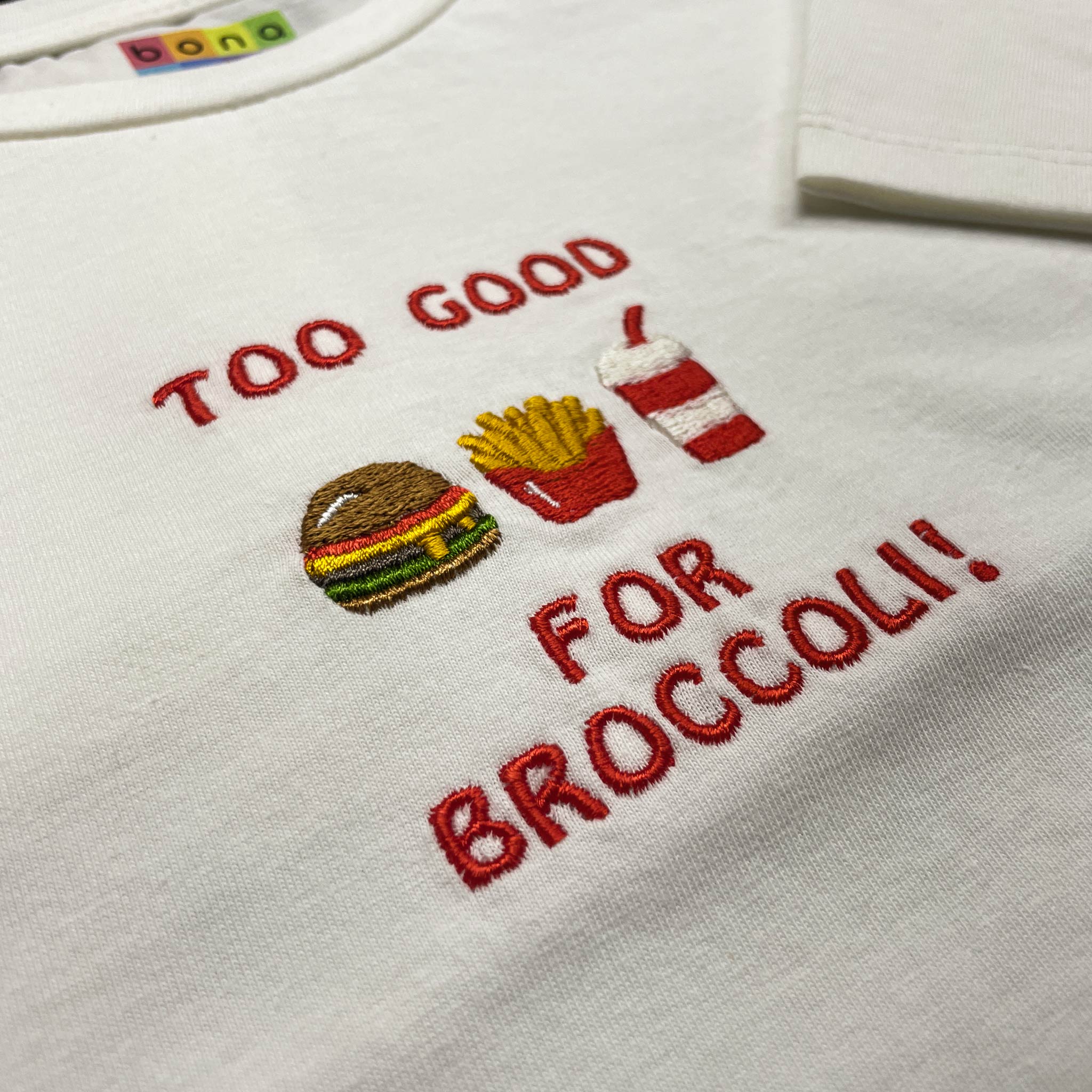 Kırık beyaz renkli %100 pamuklu çocuk oversize tişörtü. Üzerinde kırmızı iplikle işlenmiş "TOO GOOD FOR BROCCOLI!" yazısı ve renkli hamburger, patates kızartması, içecek motiflerinden oluşan nakış tasarımı yer alır. Oeko-Tex sertifikalı kumaşı nefes alan yapısıyla terletmez. Esprili premium günlük giyim parçası.