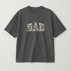 Antrasit renkli oversize tişört üzerinde, içi müşterinin gönderdiği desenli bebek kıyafeti kumaşıyla doldurulmuş ve gümüş gri iple çerçevelenmiş 'DAD' yazılı aplike nakış detayı.