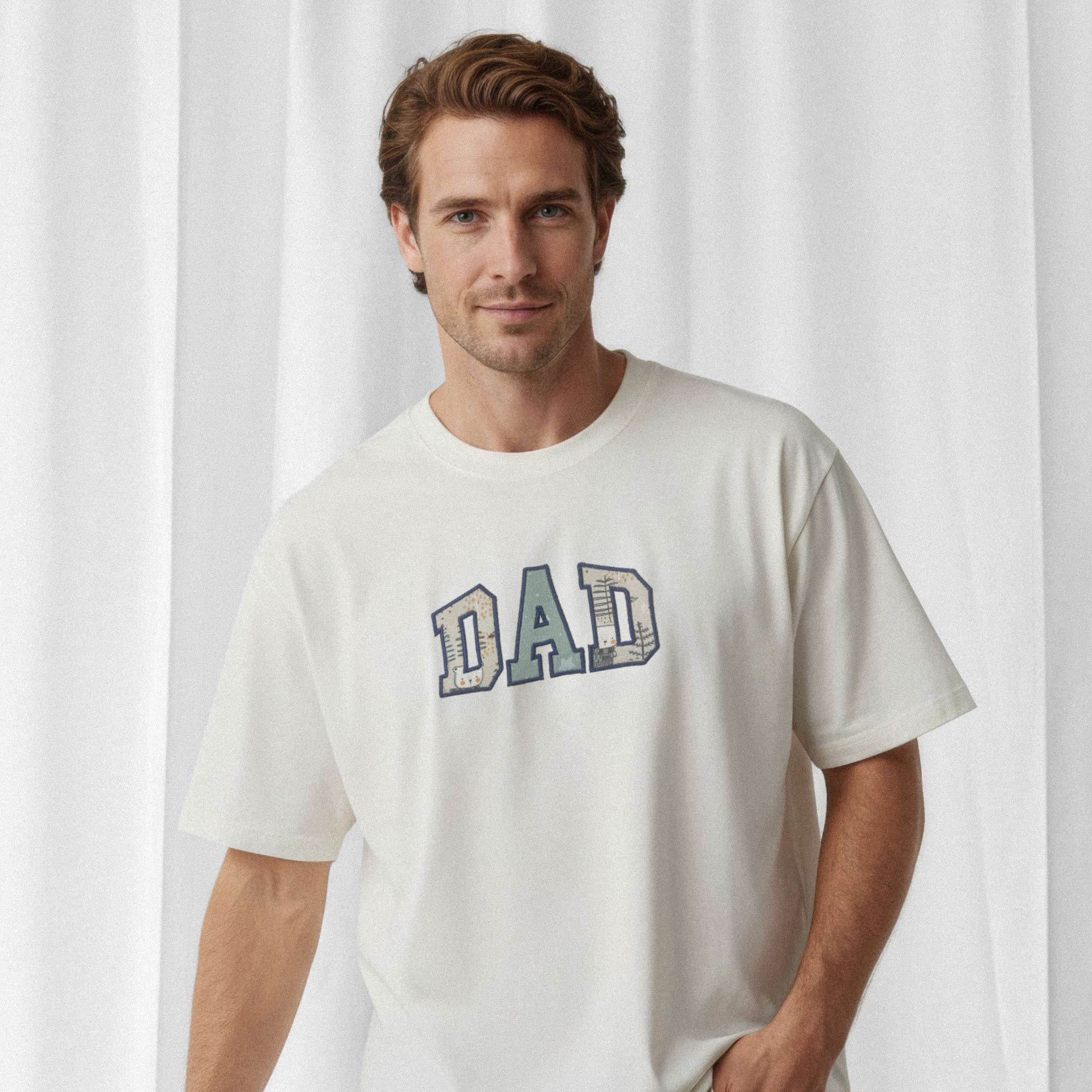 Erkek model, üzerinde Bona Pera'nın ekru renkli, kişiye özel 'DAD' aplikeli oversize tişörtü ile bir eli cebinde poz veriyor.