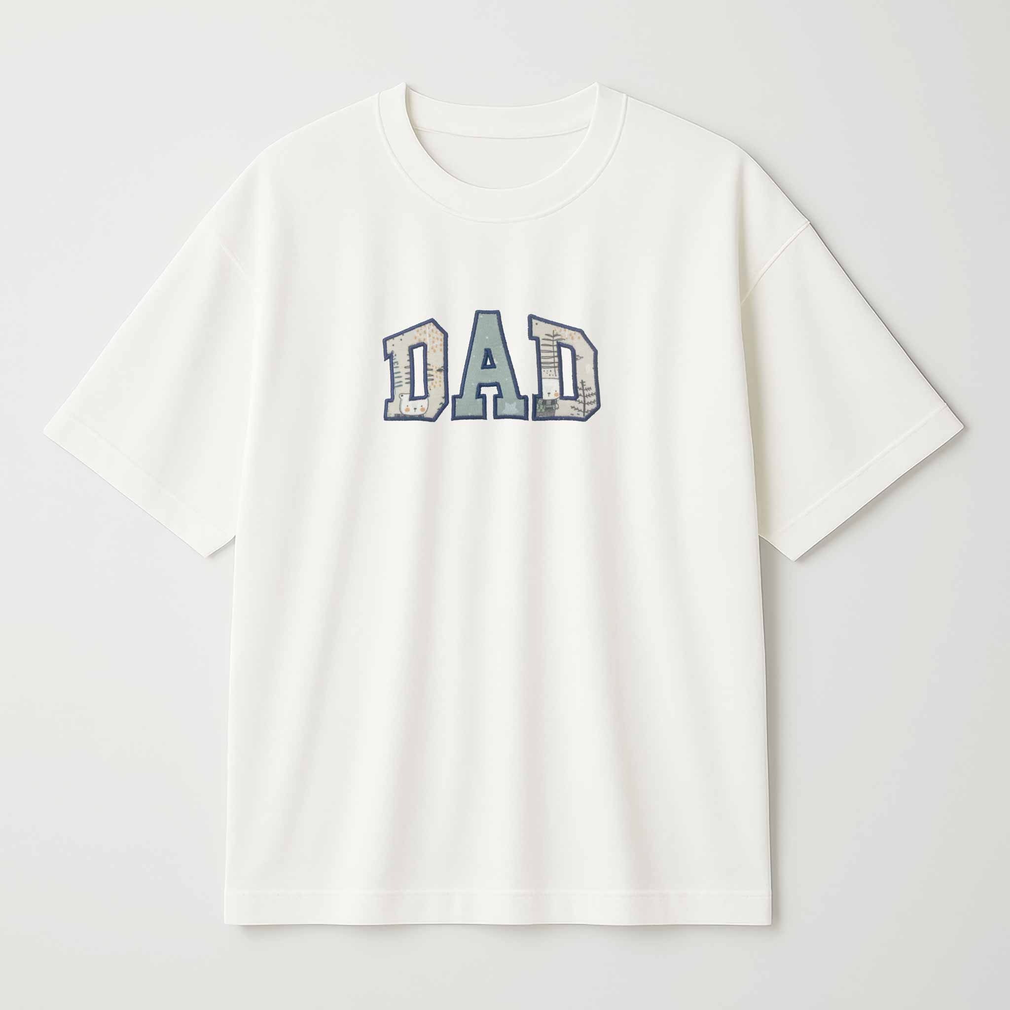 Beyaz arka plan üzerinde sergilenen, krem (ekru) renkli, oversize kesim, pamuklu "DAD" baba tişörtü. Harflerin içi, mavi ve bej tonlarında çocuk kıyafeti deseniyle kişiselleştirilmiştir.
