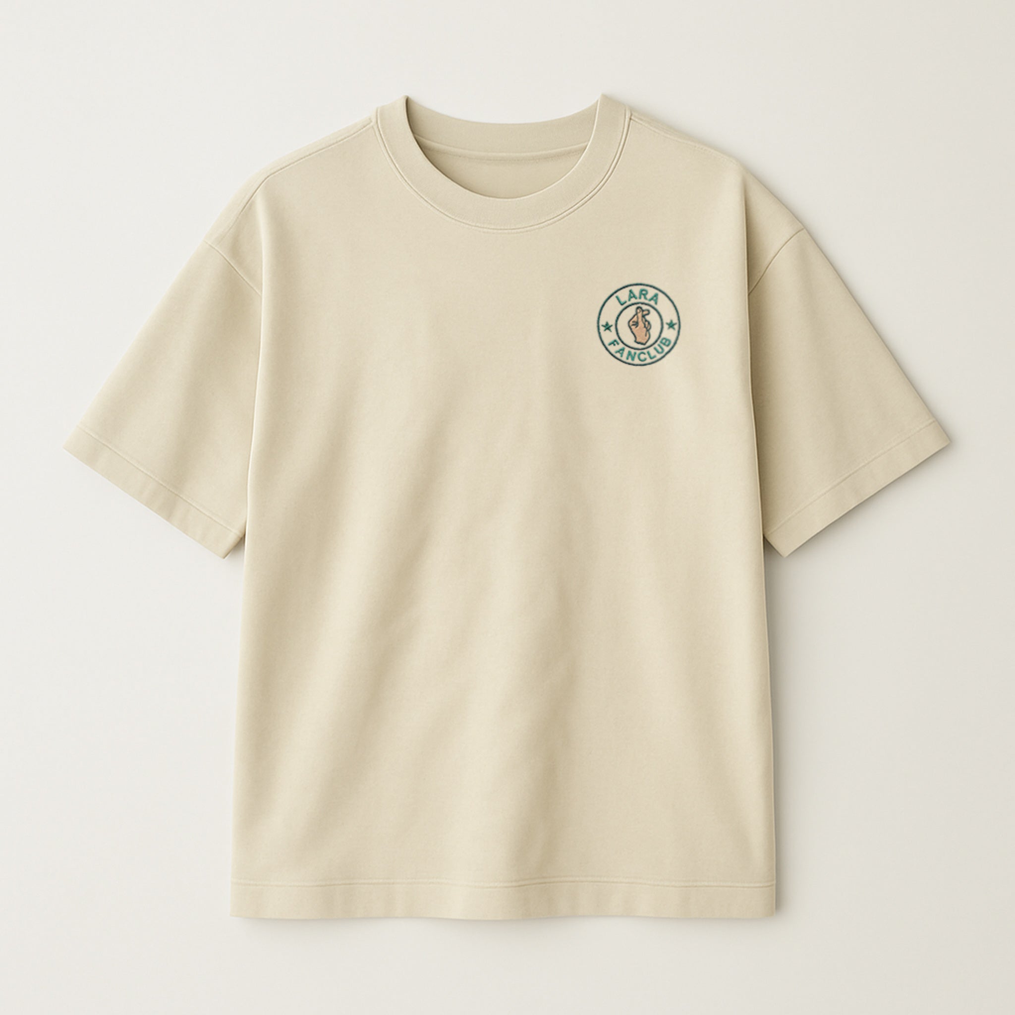 Bej renkli, oversize kesim, sol göğüs kısmında yeşil daire içinde kişiselleştirilebilir isim ve 'Fan Club' yazısı ile kalp işareti yapan el nakışı bulunan pamuklu unisex tişört.
