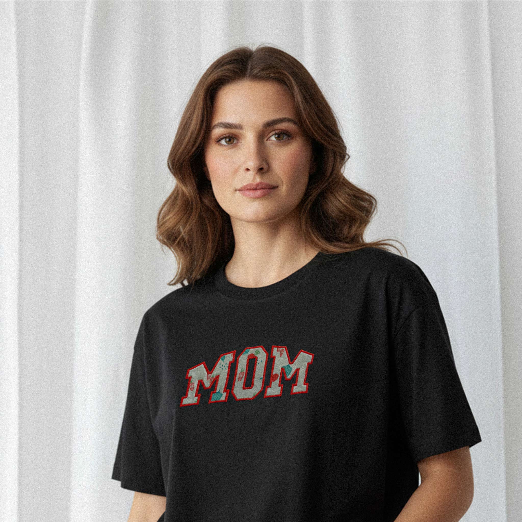 Kadın modelin üzerinde duran siyah renkli, oversize kesim, kişiye özel 'MOM' aplikeli Bona Pera anne tişörtünün yakın plan portre fotoğrafı.