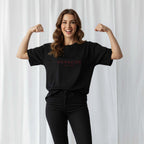 Kadın modelin üzerinde duran siyah renkli, oversize kesim, kişiye özel 'Momazing EST. [YIL]' nakışlı Bona Pera anne tişörtü. Model gülümseyerek kollarını sıkıyor.