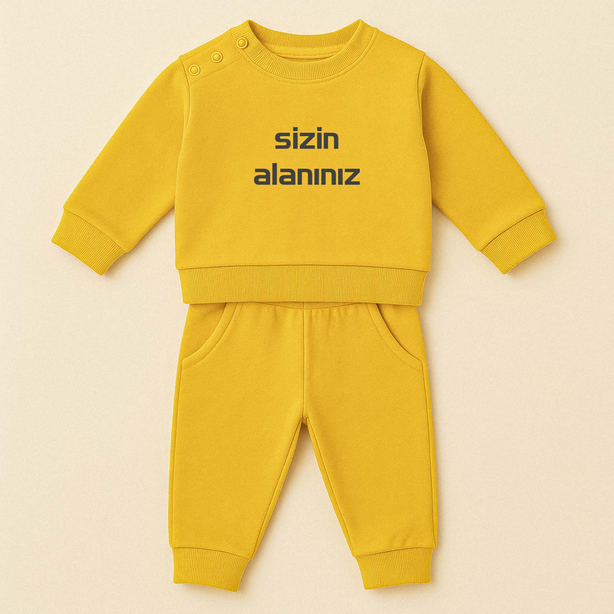 Hardal sarısı renkli, sweatshirt ve pantolondan oluşan, üzerine istenilen yazının nakışla işlenebildiği, omuzdan çıtçıtlı pamuklu bebek eşofman takımı.
