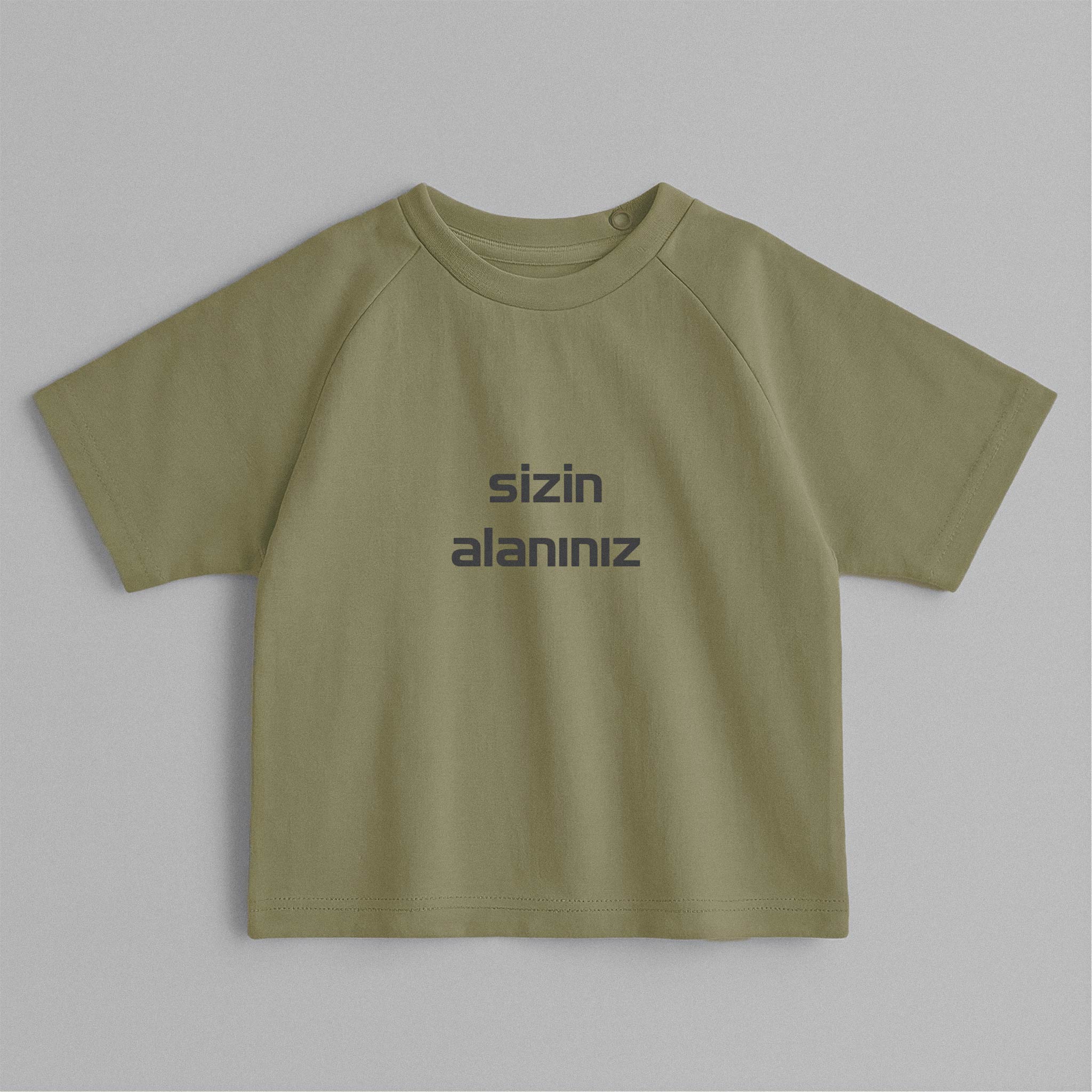 Haki yeşili, reglan kollu, omuzdan çıtçıtlı, üzerine istenilen yazının nakışla işlenebildiği pamuklu oversize bebek tişörtü.