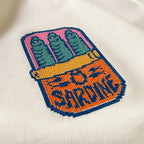 Krem renkli polar kapüşonlu sweatshirt kumaşı üzerine işlenmiş retro pixel art temalı "Sardine" (sardalya konservesi) nakışının makro (yakın çekim) detayı. Görselde kanaviçe (cross stitch) tekniği görünümüyle, piksel piksel işlenmiş renkli sardalya figürünün ve "SARDINE" yazısının şardonlu tok kumaş üzerindeki çarpıcı dokusu net bir şekilde görülmektedir. Birinci sınıf Alman nakış ipliği kullanılarak yüksek hassasiyetle işlenmiş, eğlenceli ve premium tasarımın yüksek çözünürlüklü detay karesi.