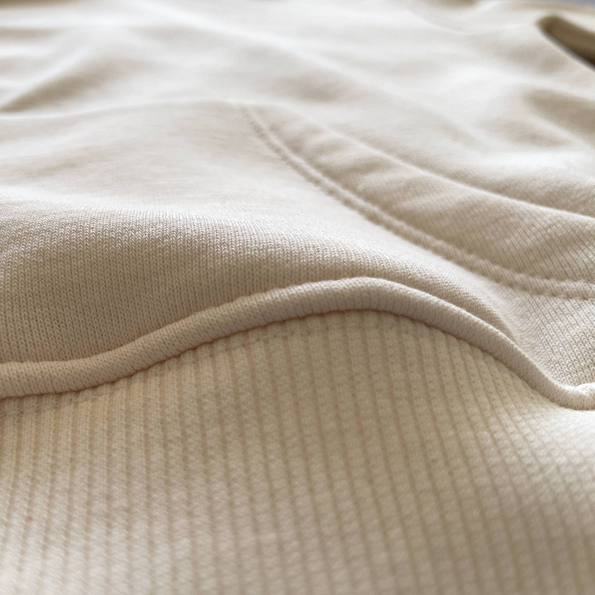 Krem renkli şardonlu çocuk hoodie modelinin kanguru cep birleşim yerindeki kusursuz ve sağlam üst dikişlerini gösteren detay fotoğrafı. Çocukların dışarıda güvenle oyun oynarken ellerini ısıtabileceği pratik cep tasarımı. Nefes alan pamuklu yapısı ve soğuğu geçirmeyen kalın kışlık kumaşıyla Oeko-Tex onaylı bu çocuk sweatshirt, formunu koruyan esnek dokusuyla soğuk havalarda maksimum rahatlık sağlar. Terletmeyen iç yüzeyi sayesinde hareketli çocukların kışlık gardırobu için ideal bir parçadır.