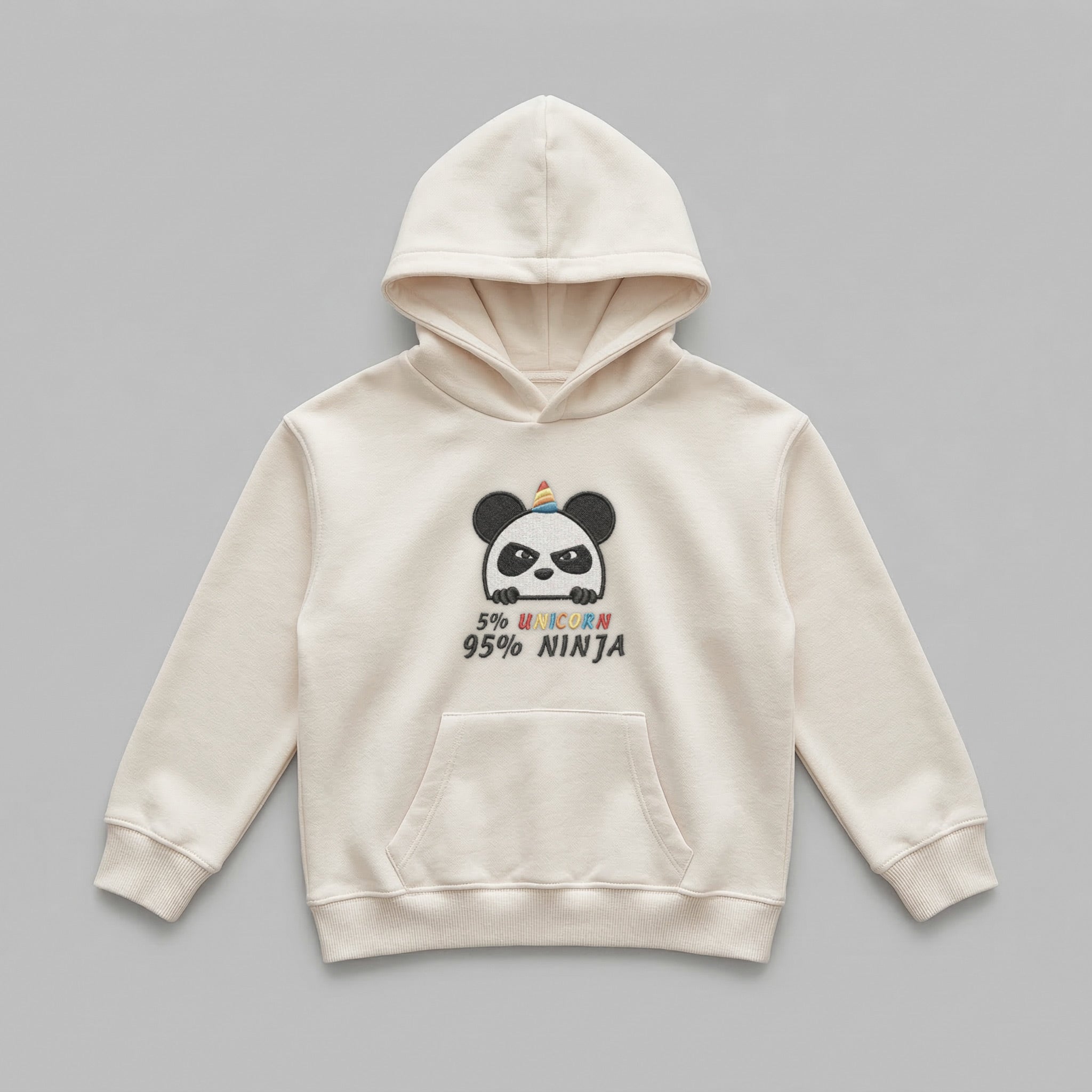 2-7 yaş çocuklara özel krem renkli kapüşonlu sweatshirt önden görünümü. Göğsünde esprili '5% UNICORN, 95% NINJA' yazısı ve sevimli panda nakışı bulunur. %65 pamuklu şardonlu iç dokusu kışın terletmeden sıcak tutar. Oeko-Tex sertifikalı bu çocuk hoodie, geniş kanguru cebi ve esnek manşetleriyle hareket özgürlüğü sağlar. Sağlıklı, kaliteli ve dayanıklı kışlık üst giyim arayan ebeveynler için ideal, rüzgarı kesen pürüzsüz pamuklu dış yüzeye sahip premium bir tasarımdır.