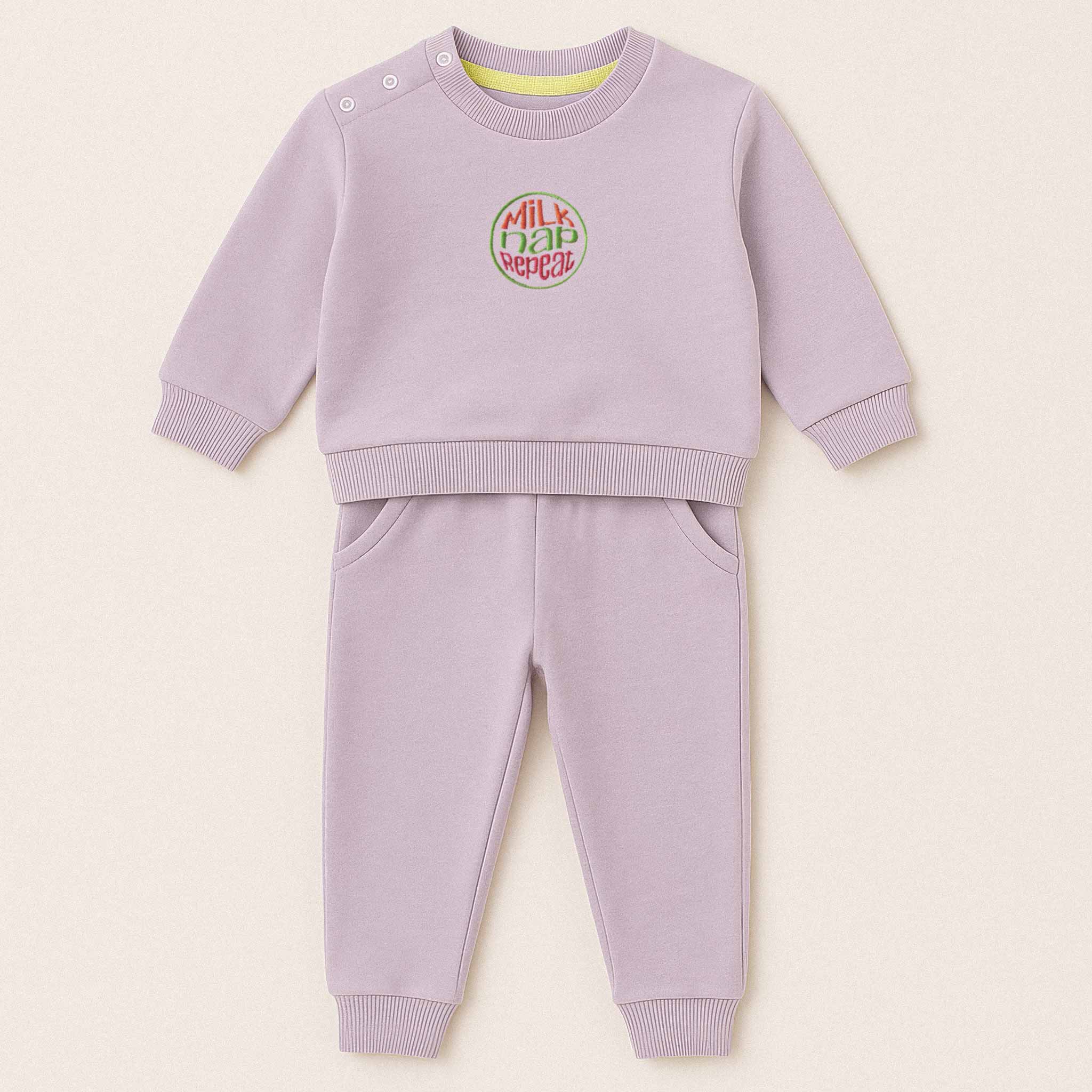 Lila (leylak) renkli, sweatshirt ve pantolondan oluşan, üzerinde "Milk Nap Repeat" baskısı bulunan, omuzdan çıtçıtlı pamuklu bebek eşofman takımı.
