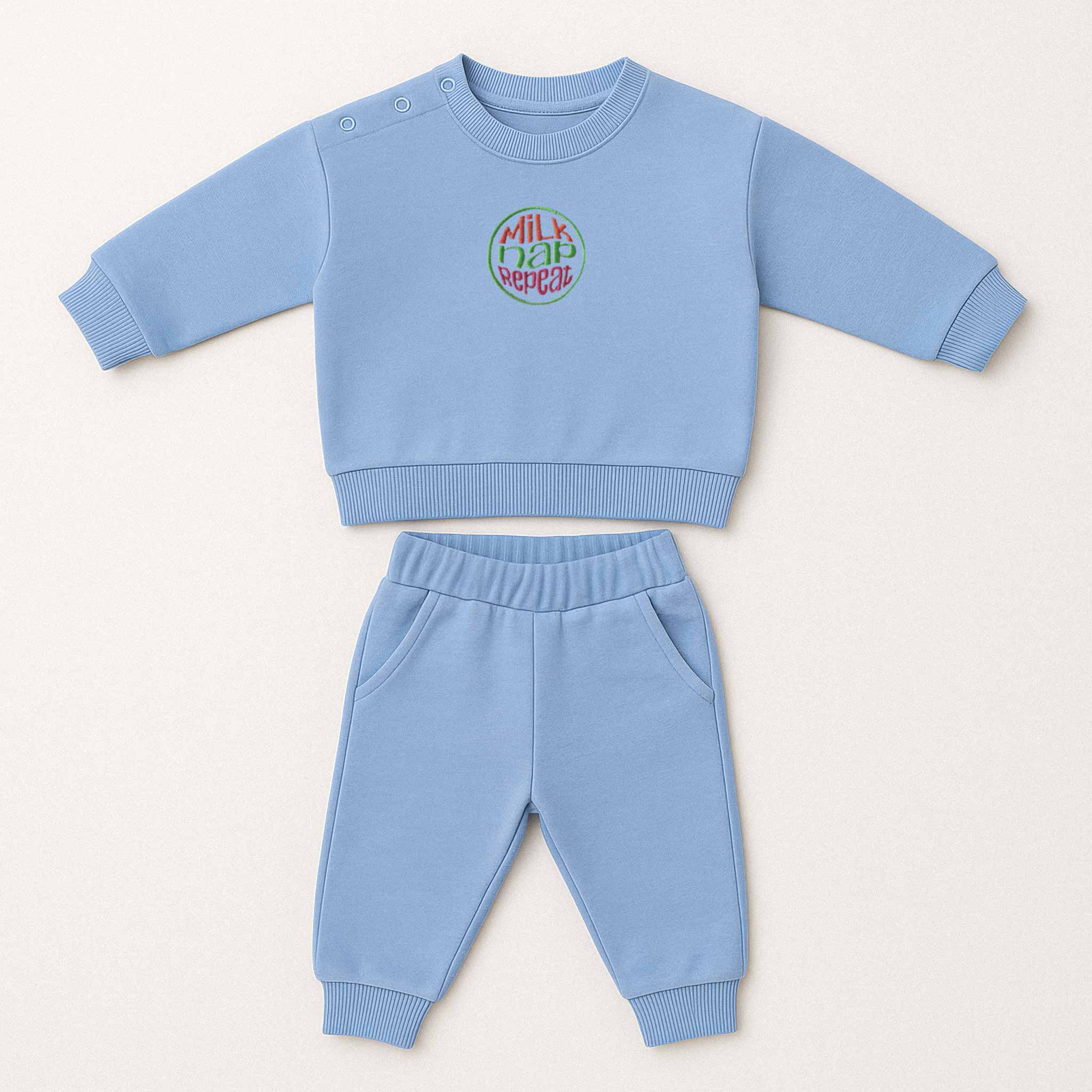 Mavi renkli, sweatshirt ve pantolondan oluşan, üzerinde "Milk Nap Repeat" baskısı bulunan, omuzdan çıtçıtlı pamuklu bebek eşofman takımı.