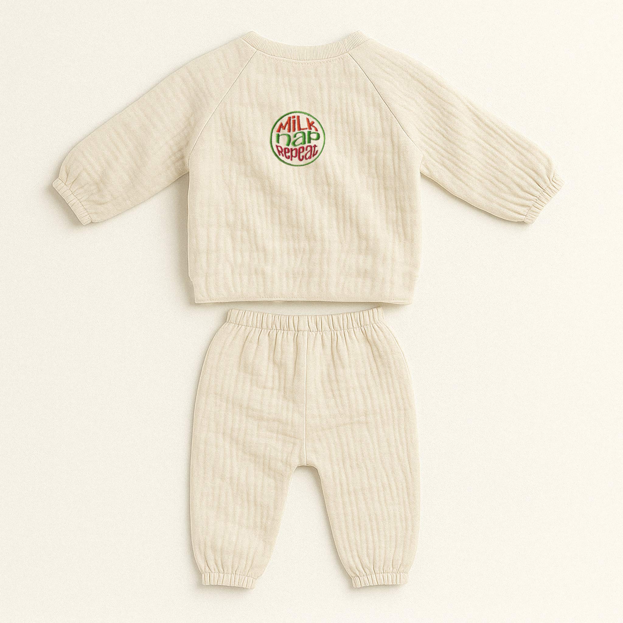 Doğal bej (ekru) renginde, müslin kumaştan yapılmış, üzerinde "Milk Nap Repeat" baskısı bulunan, yandan bağlamalı kimono üst ve pantolondan oluşan yenidoğan bebek takımı.