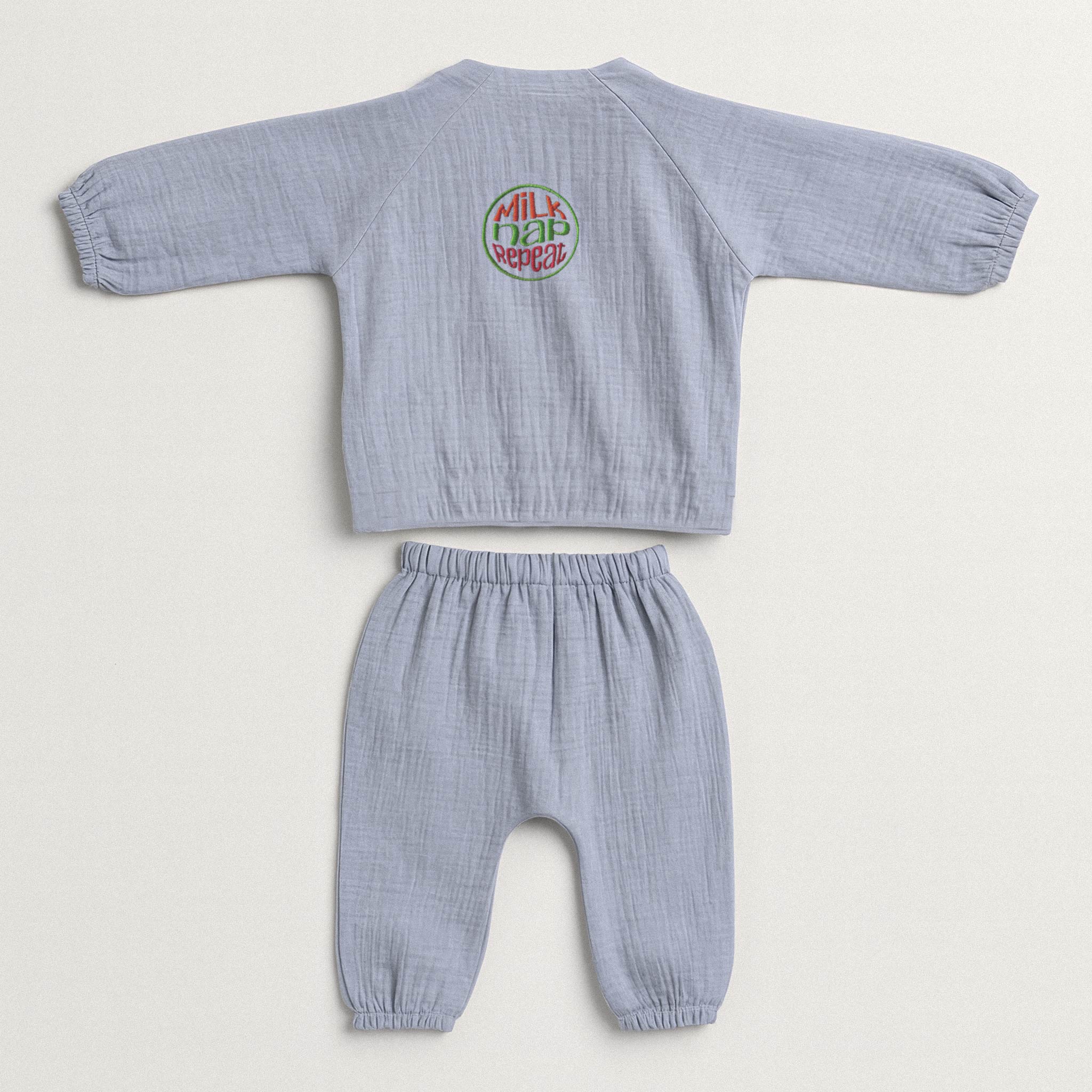 İndigo mavisi renginde, müslin kumaştan yapılmış, üzerinde "Milk Nap Repeat" baskısı bulunan, yandan bağlamalı kimono üst ve pantolondan oluşan yenidoğan bebek takımı.