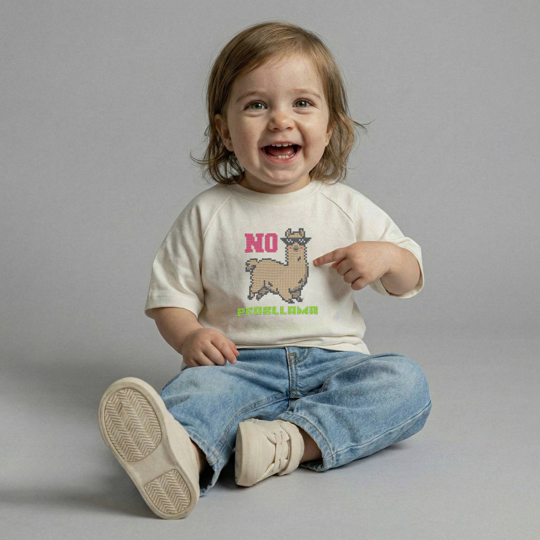 Ekru renkli, üzerinde pikselli lama nakışı bulunan tişört giyen ve neşeyle tişörtündeki lamayı işaret eden kız bebek model.