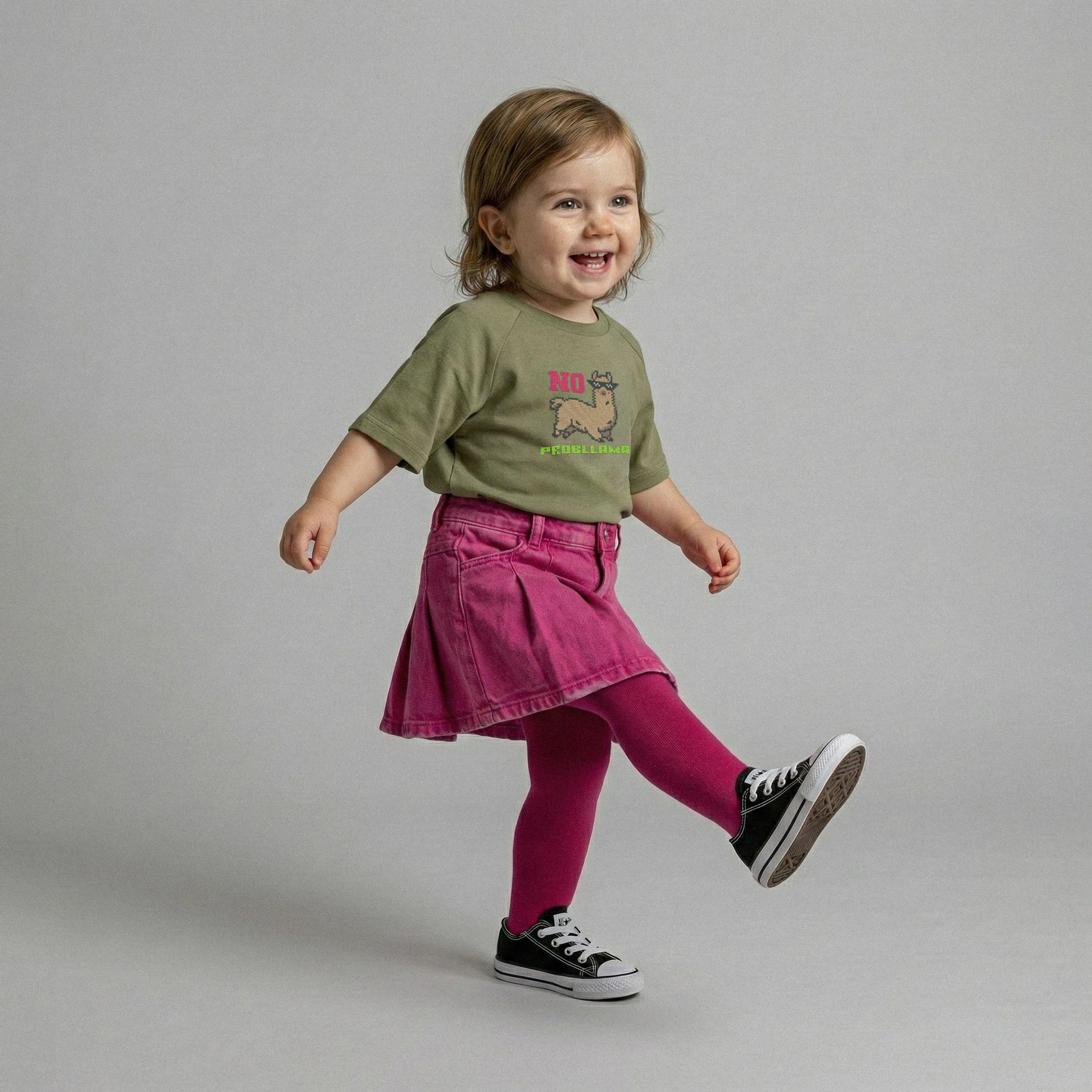 Haki yeşili, lama nakışlı tişört ve pembe etek giyen, ayağını kaldırıp adım atarken neşeyle gülümseyen kız bebek model.
