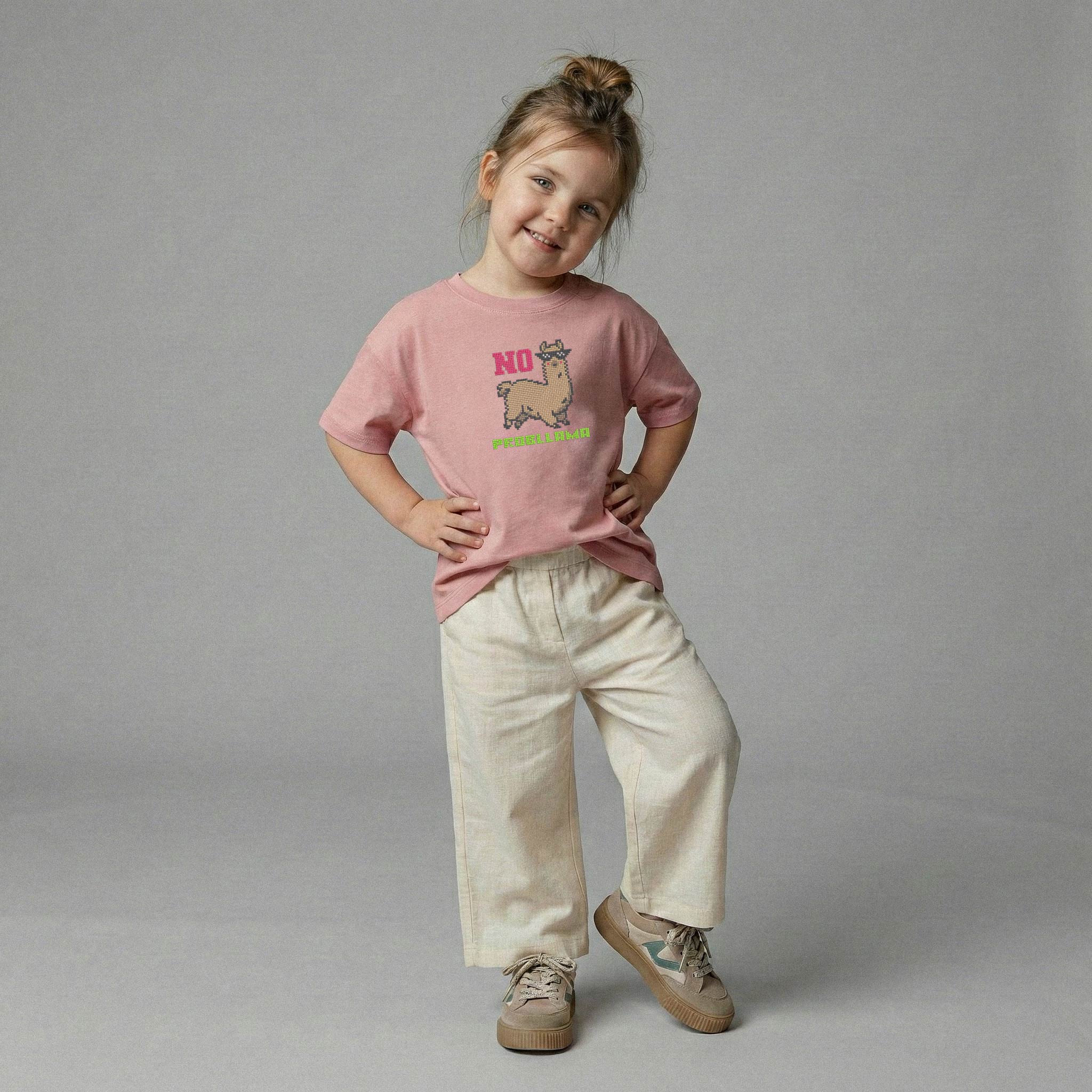 Gül kurusu rengi, lama nakışlı oversize tişört ve açık renk bol pantolon giyerek elleri belinde poz veren gülümseyen kız çocuk model.